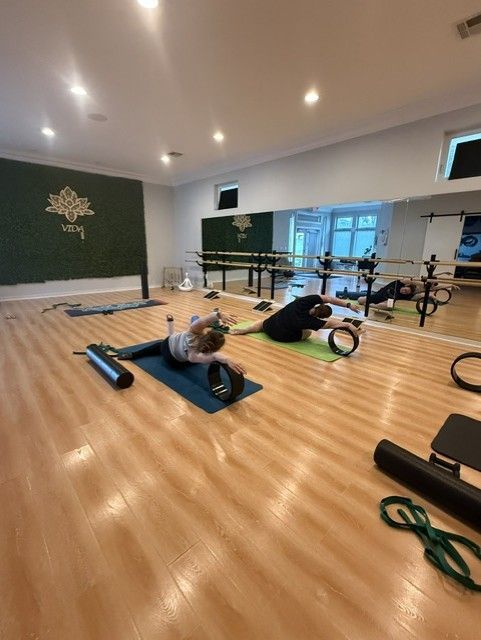 Yoga studio with two people doing floor exercises on mats beside ballet barres
