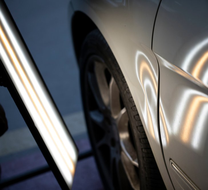 Dent repair on a white car, using a reflection board to detect dents.