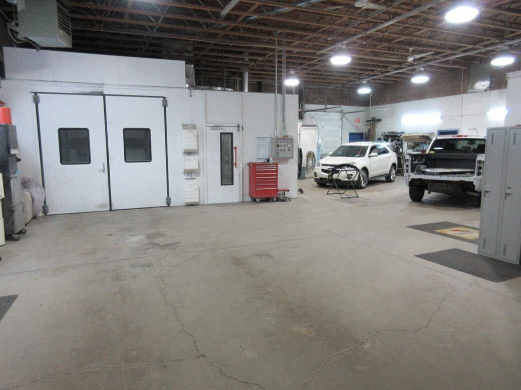 A garage interior with a paint booth, white SUV, and pickup truck.