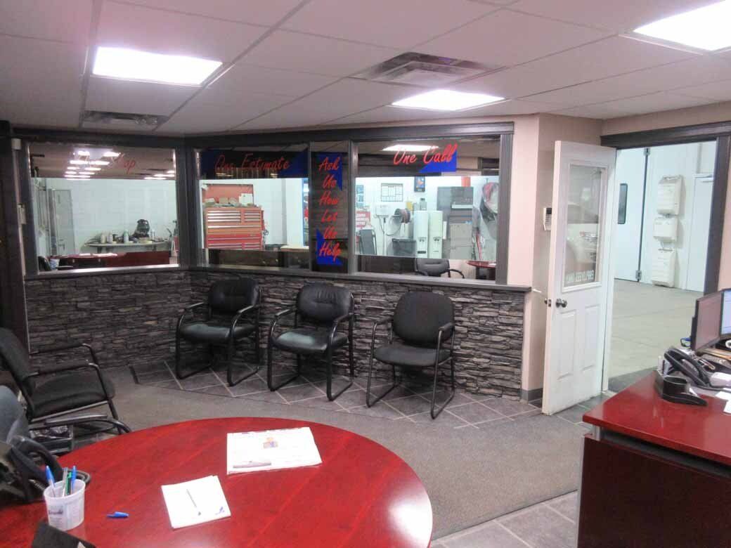Waiting room with a red circular table, black chairs, and a doorway. The area is lit by overhead lights.