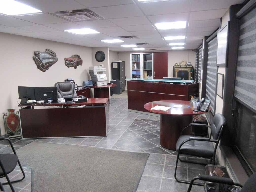 Office interior with desks, chairs, and a round table. Dark wood furniture and gray tiled floor.