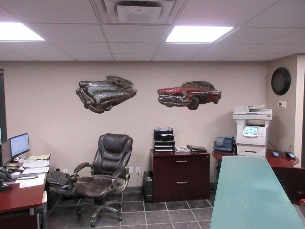 Office interior with car-themed wall art, desk, chair, printer, and filing cabinet.