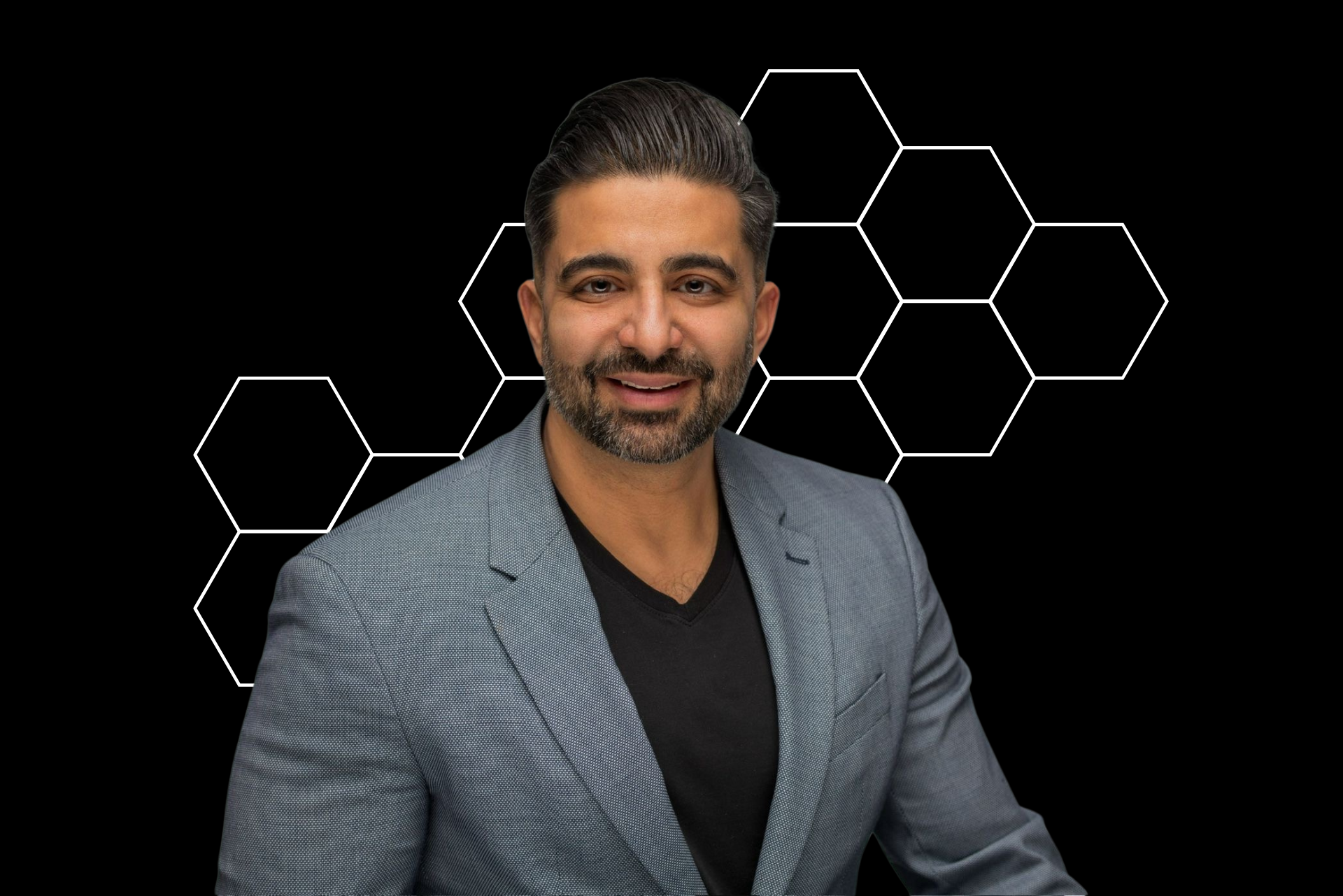 A man in a suit and black shirt is standing in front of a black background.