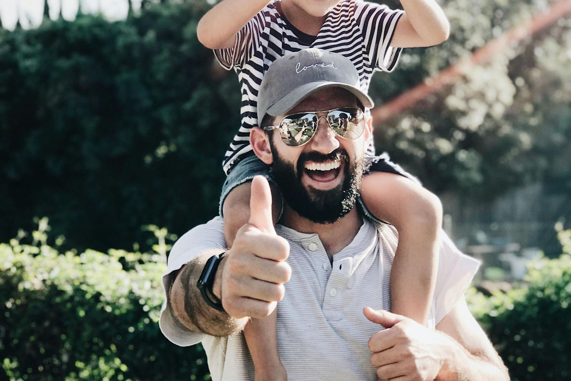 A man is carrying a child on his shoulders and giving a thumbs up.