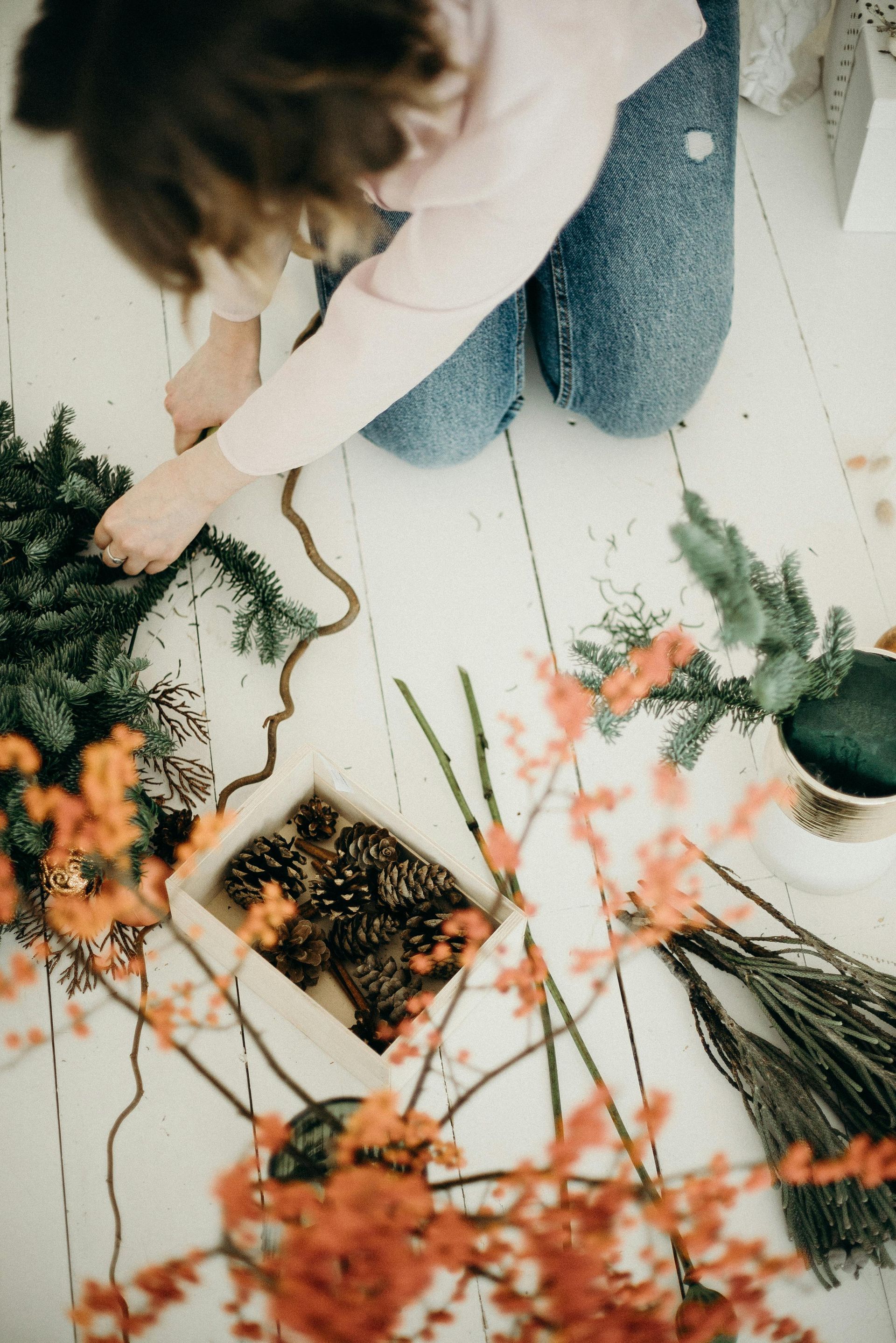 A woman is kneeling on the floor making a christmas wreath.