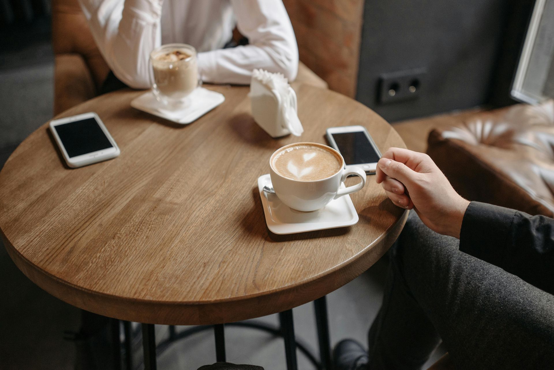 Two people are sitting at a table with cups of coffee and phones.