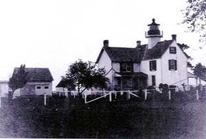 A vintage black-and-white photo of a two-story lighthouse residence with a small, detached outbuilding.