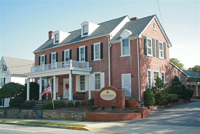 A brick two-story inn with a white pillared porch, dormer windows, and a prominent sign in its front yard.