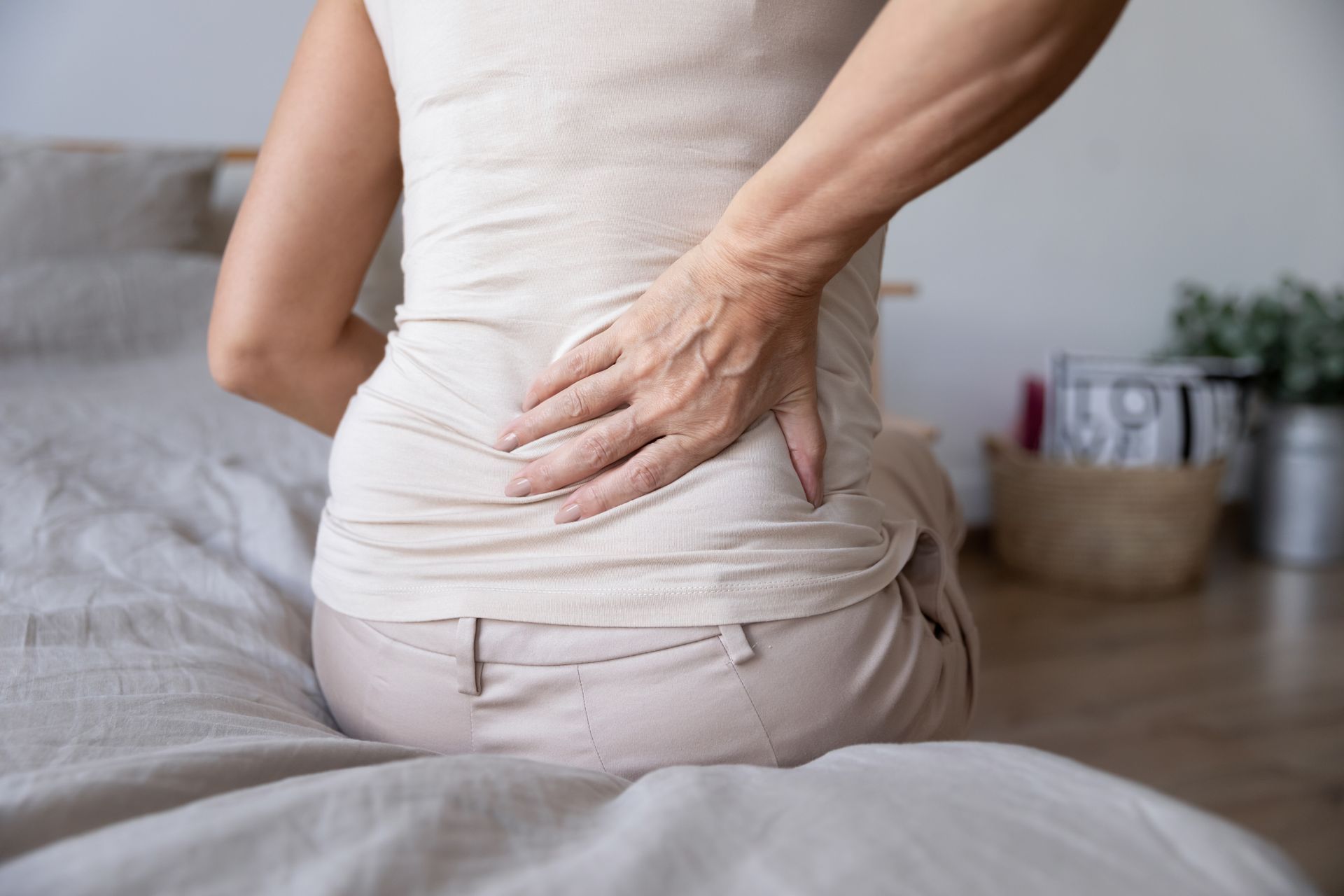 Person holding their lower back while sitting on a bed, suggesting back pain