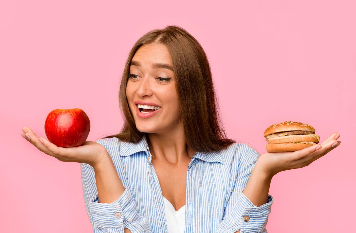 Woman weighing an apple and a burger against a pink background
