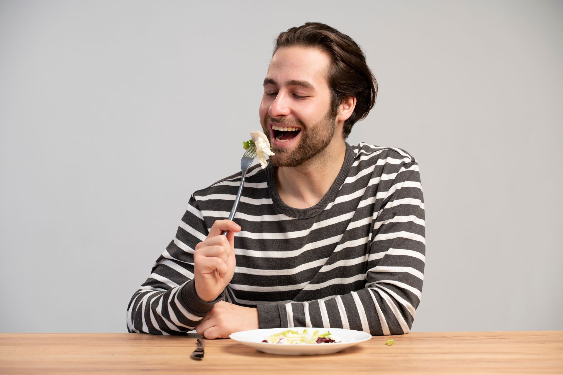 A man is sitting at a table eating a salad with a fork.