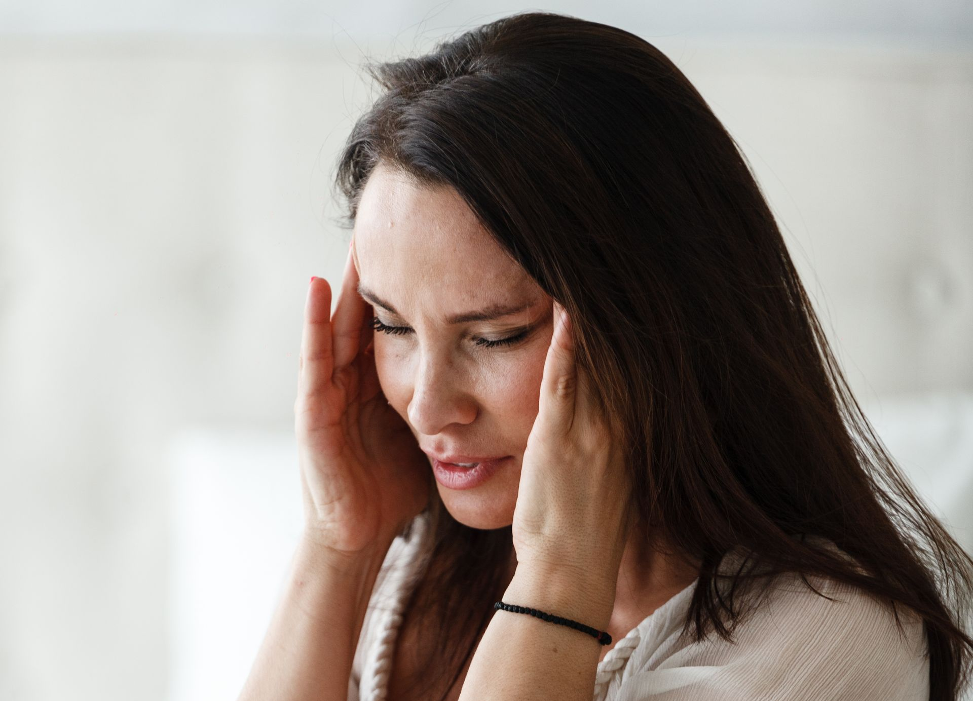 Woman with dark hair holding her temples, showing a pained expression.