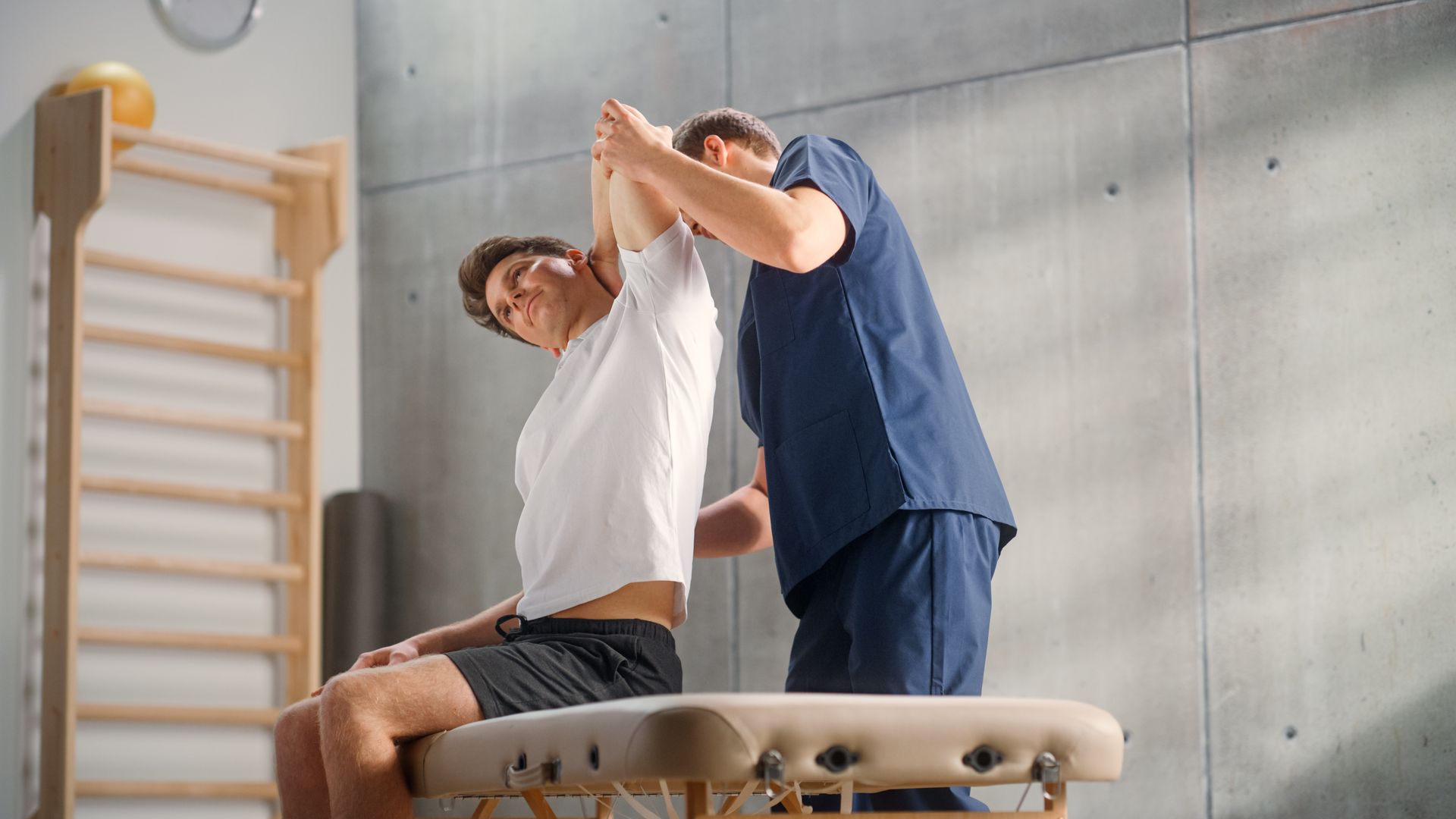 Physiotherapist stretching a seated patient's arm in a clinic.