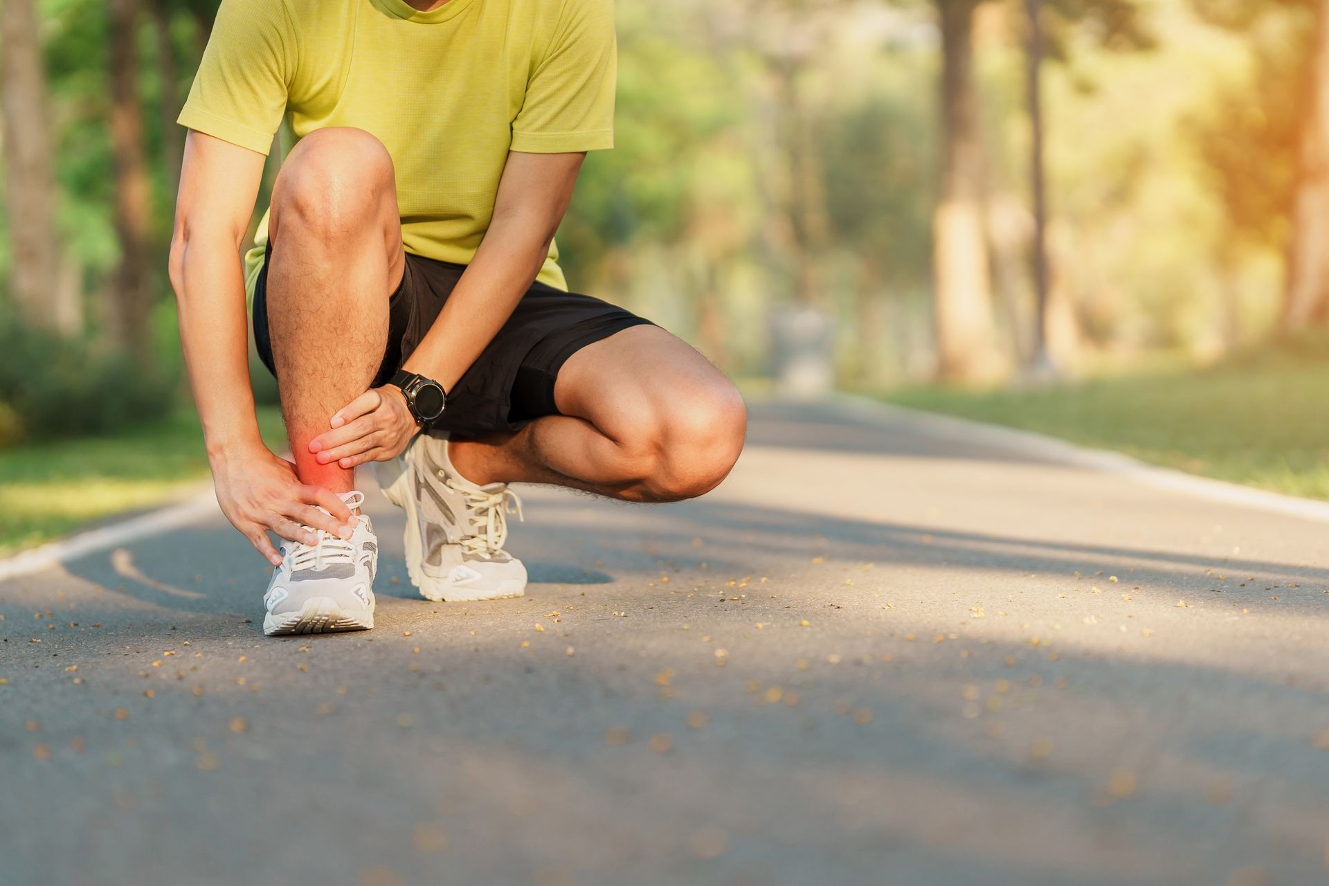 Man on a path, holding his ankle in pain. Wearing running clothes.