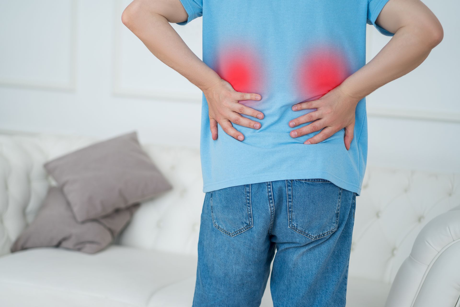 Person with hands on lower back, indicating pain, with red highlights over kidneys, indoors.