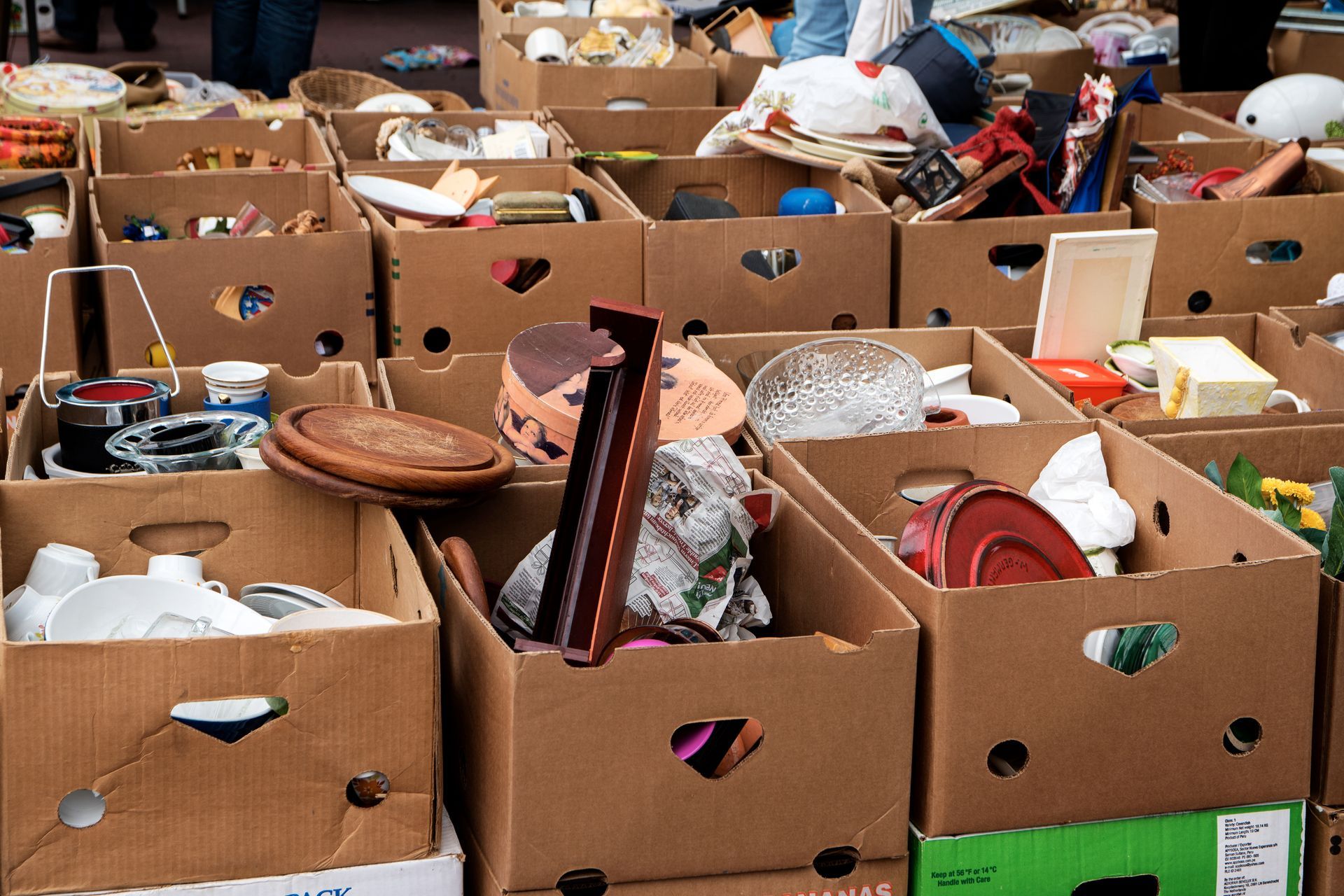 Cardboard boxes overflowing with items at a flea market, outdoors.