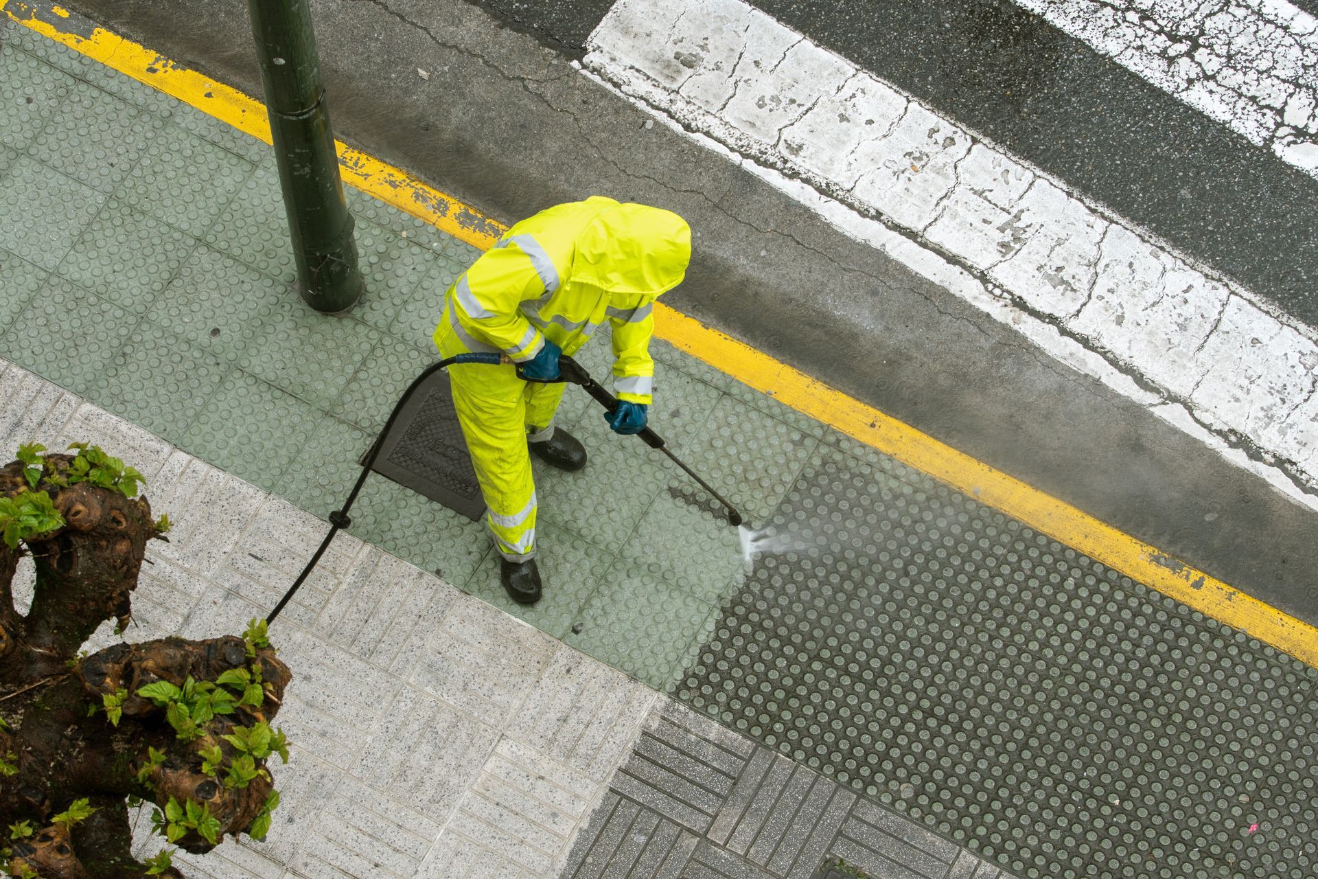 Person in yellow protective suit sprays a sidewalk with a high-pressure hose. Person in yellow protective suit sprays a sidewalk with a high-pressure hose.