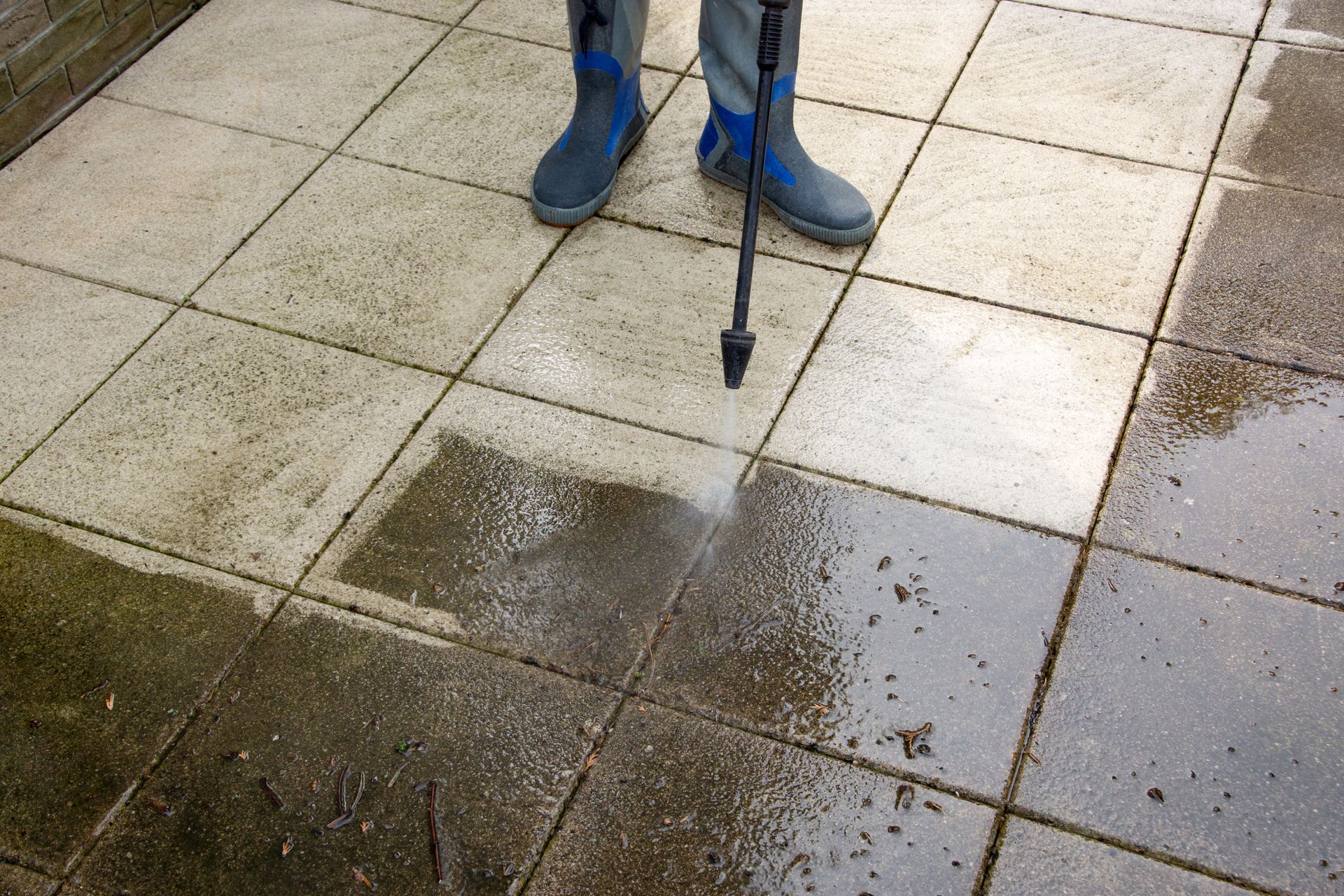 Person pressure washing a dirty, mossy tiled patio. Person pressure washing a dirty, mossy tiled patio.