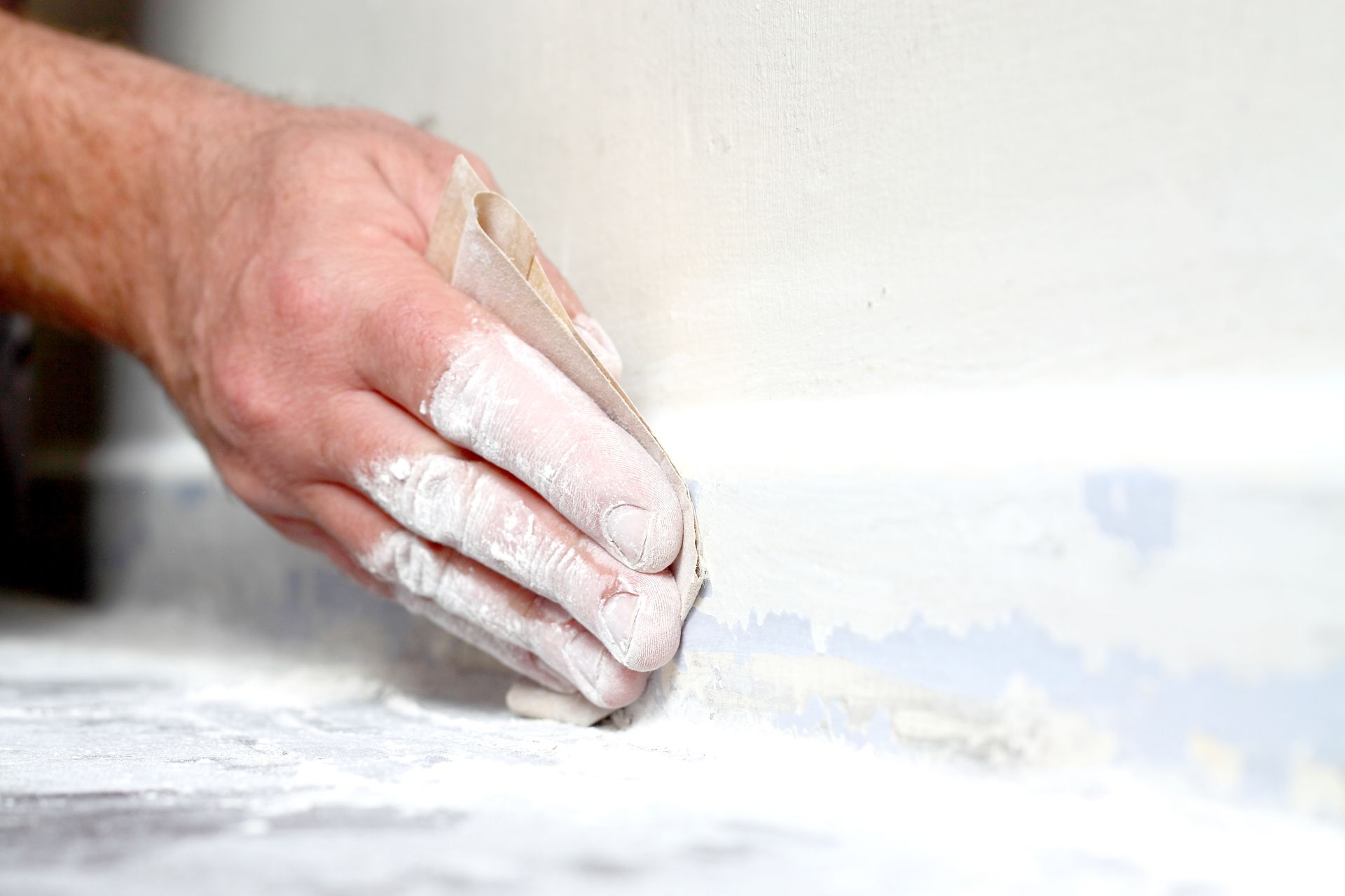Hand sanding a white wall with a sanding block, creating dust on the wall and floor. Hand sanding a white wall with a sanding block, creating dust on the wall and floor.