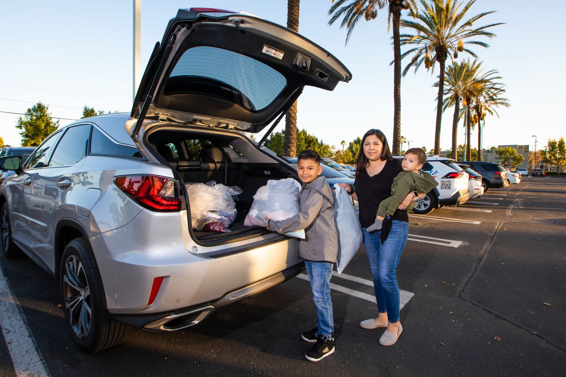 People loading bags into the open trunk of a silver SUV in a parking lot at sunset