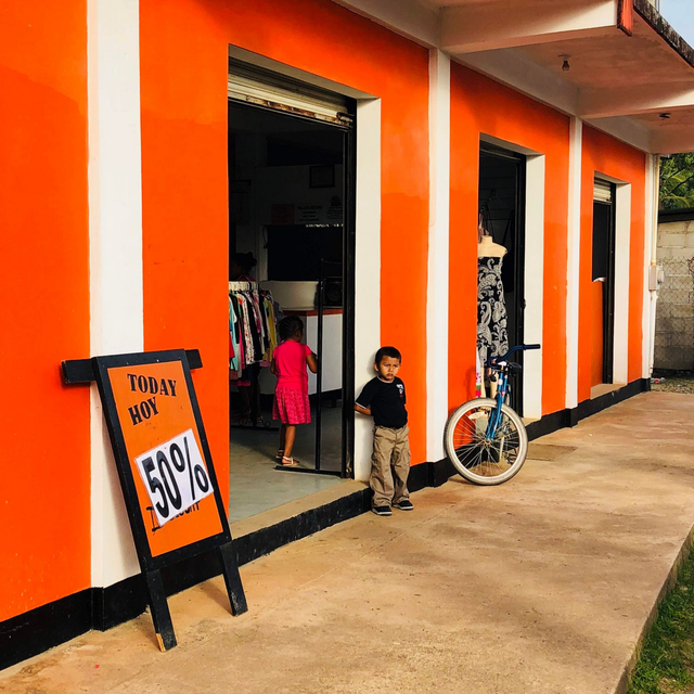 Orange storefront with sale sign, two children at the entrance, and a bicycle leaning nearby