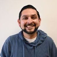 Smiling person in a blue hoodie against a plain light wall