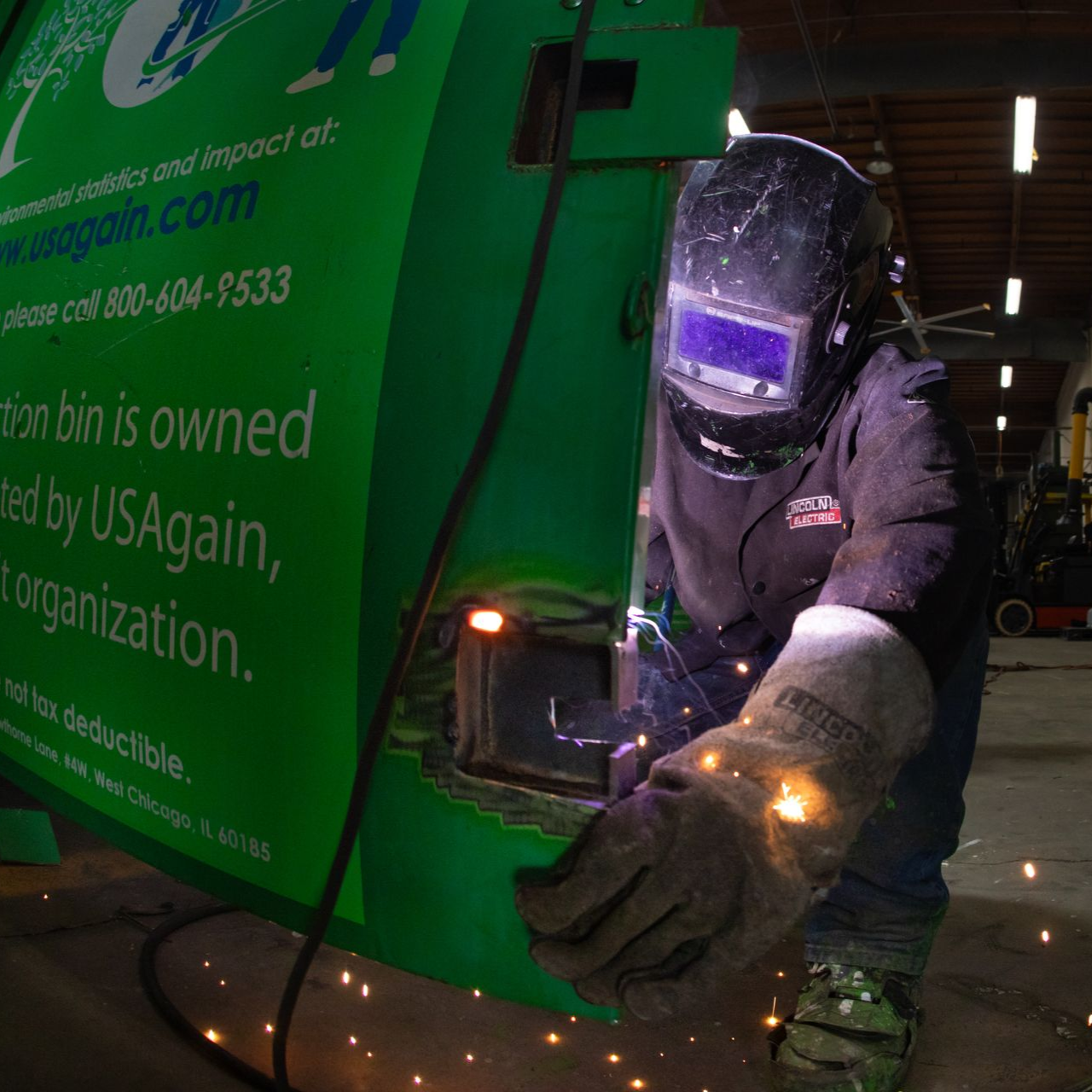 Welder repairing a green garbage truck at night, sparks flying from the metal frame.