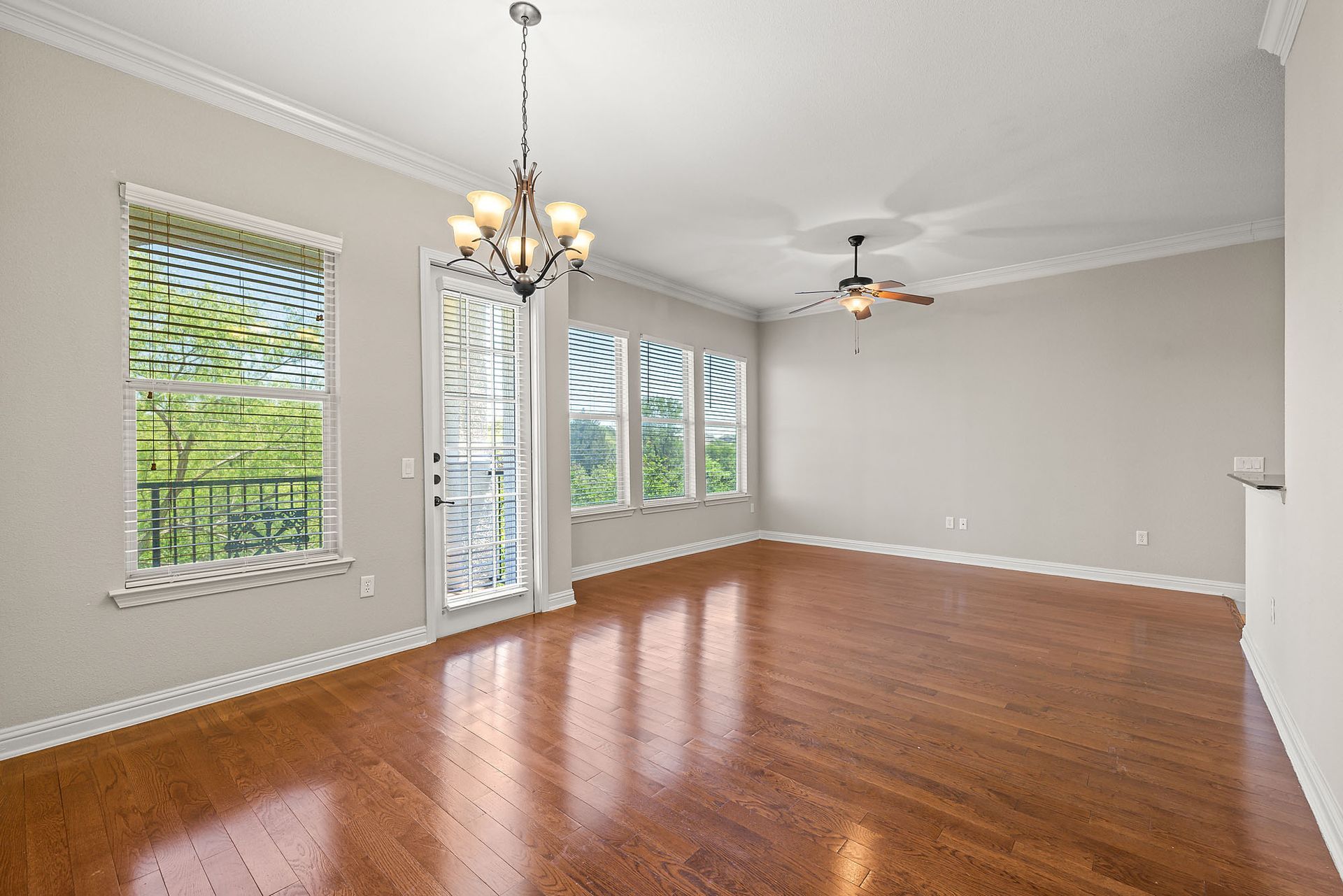Empty living room with wood flooring, several windows, and a chandelier, offering views of greenery at Marquis at TPC, offers San Antonio apartments for rent. 