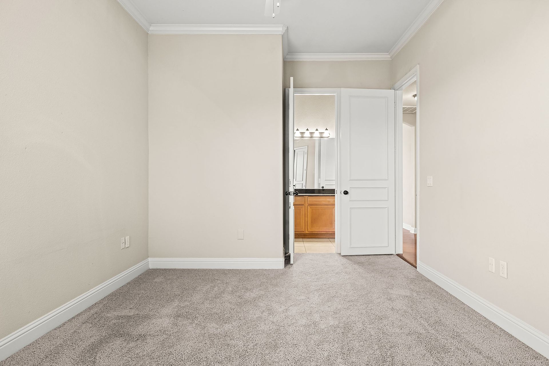 Empty beige bedroom with a bathroom visible through an open door at Marquis at TPC, offers pet-friendly apartments in San Antonio, TX. The room has carpet and simple molding.