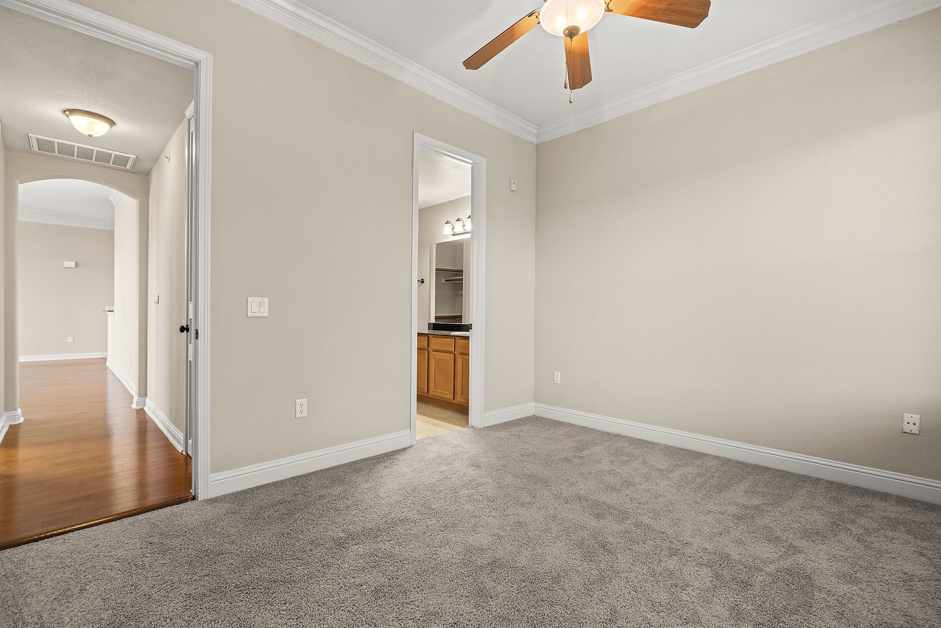 Bedroom with neutral walls, gray carpet, and an adjoining bathroom. Hallway visible through the door on the left at Marquis at TPC, offers pet-friendly apartments in San Antonio, TX.