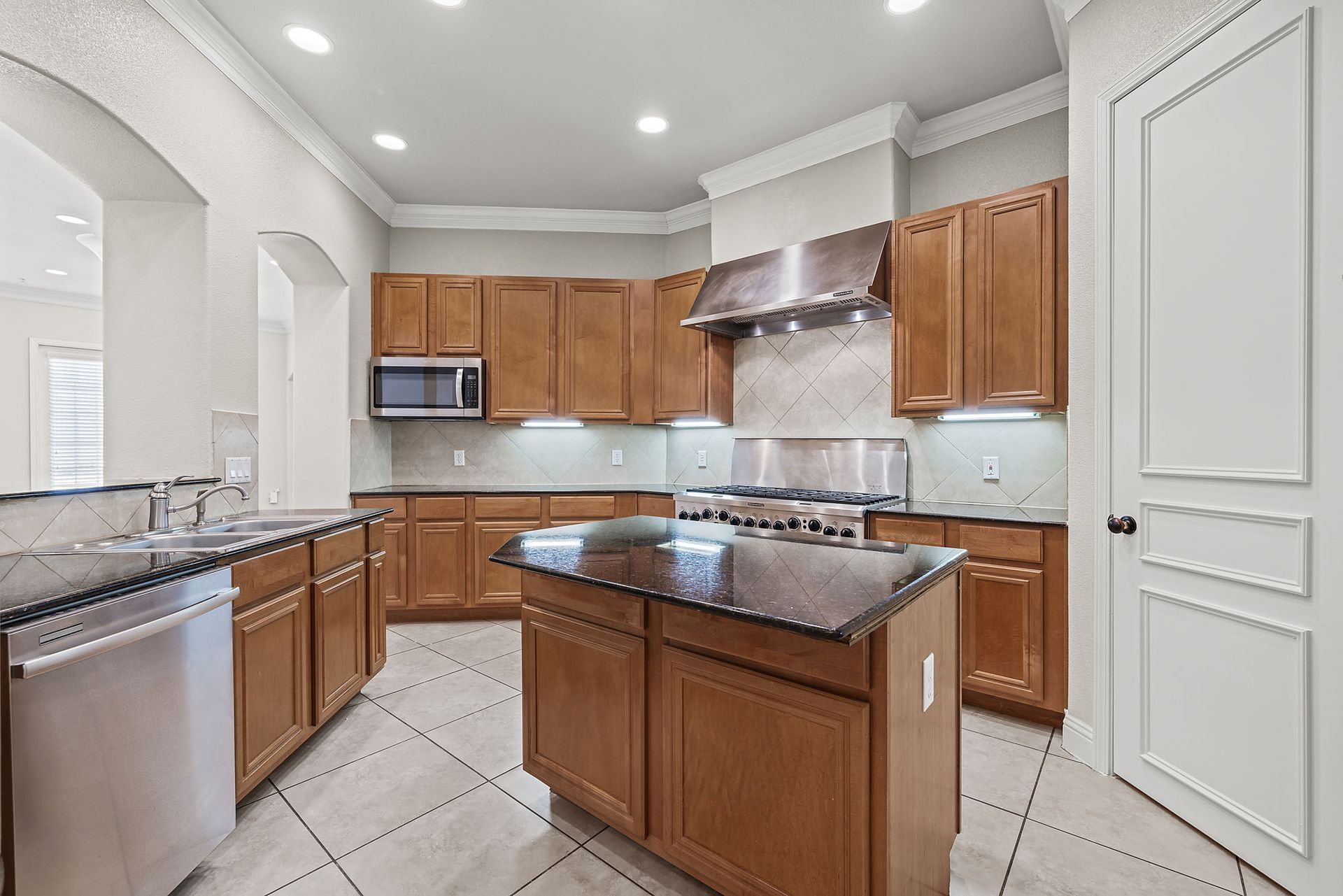 A spacious kitchen featuring brown cabinets, a dark island, stainless steel appliances, and light-colored tiled flooring at Marquis at TPC, offers apartments for rent in San Antonio, TX.