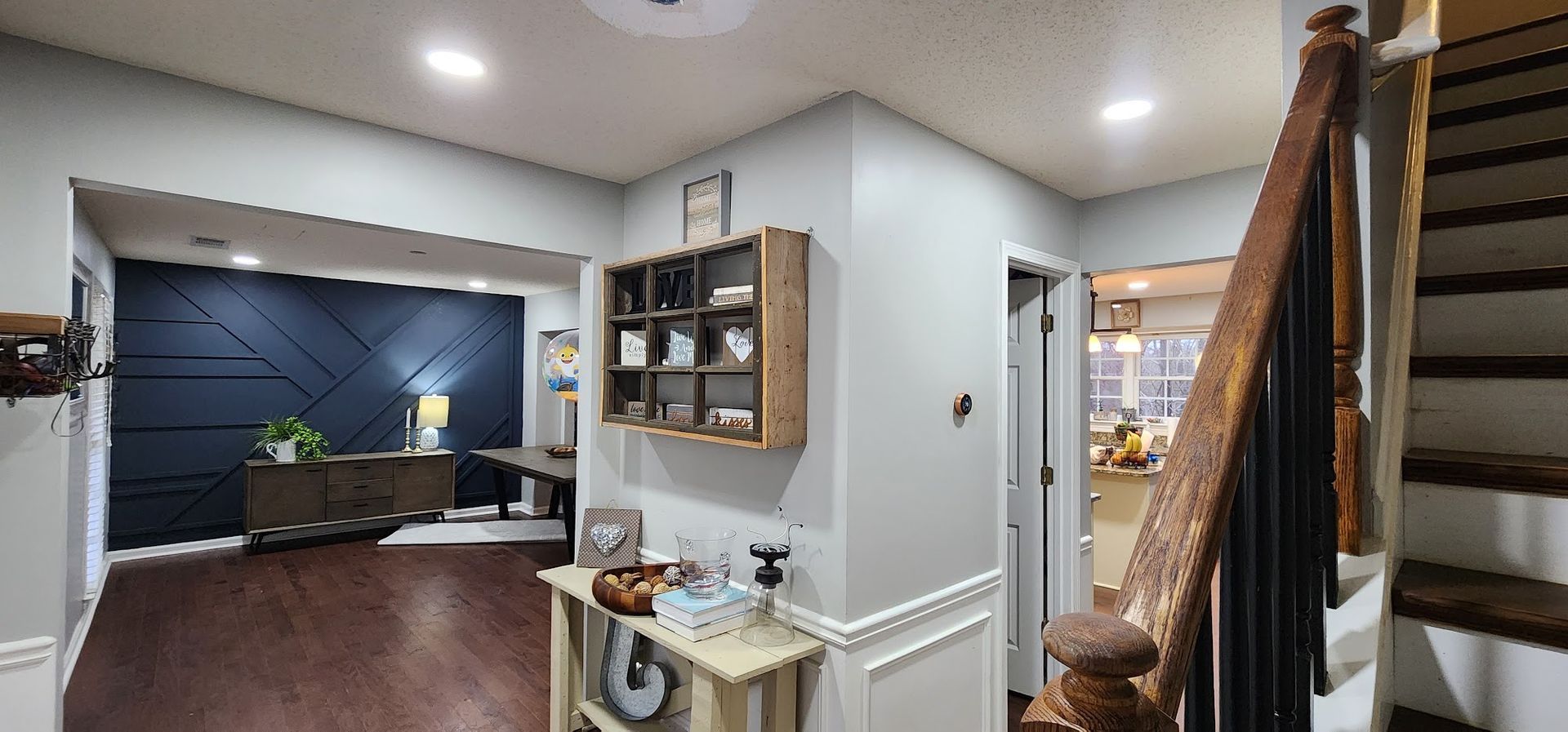 Hallway view into a home office with dark accent wall, desk, shelves, and a staircase on the right
