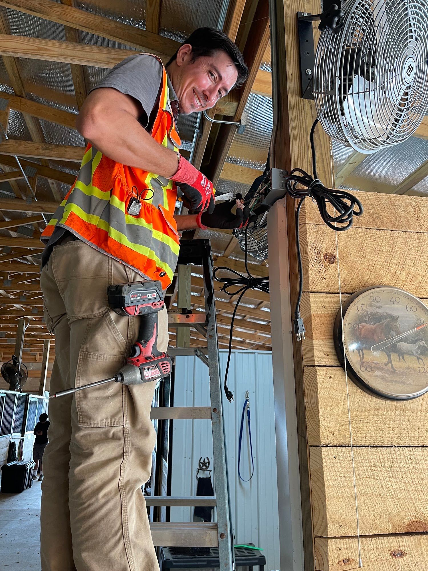 Worker in orange safety vest wiring cables on a ladder in a utility area