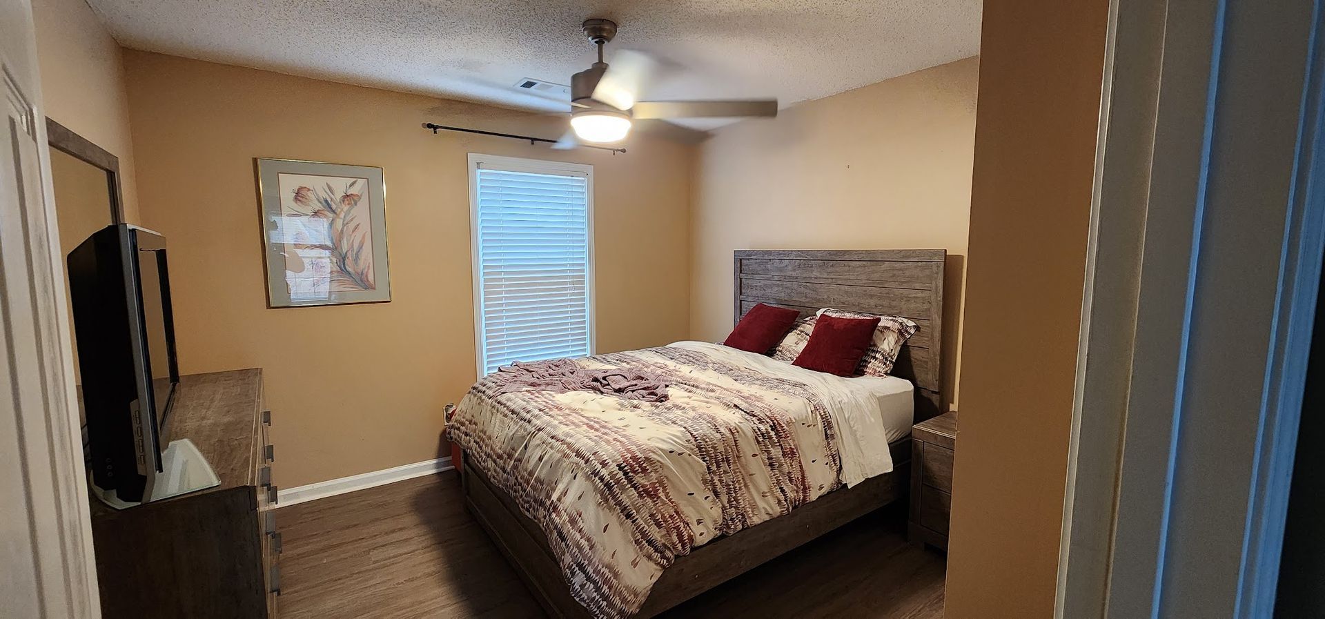 Bedroom with a bed, ceiling fan, window, dresser, and wall art in a beige room