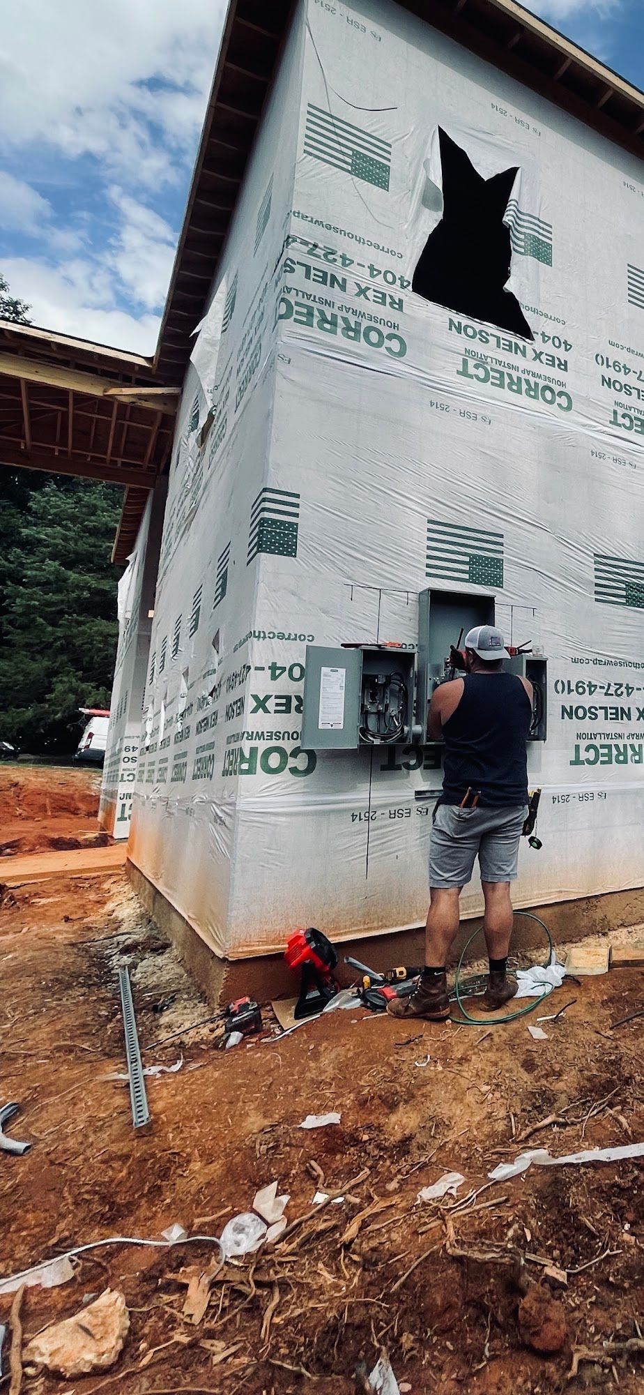 Worker installing exterior wrap on a house under construction on a muddy lot