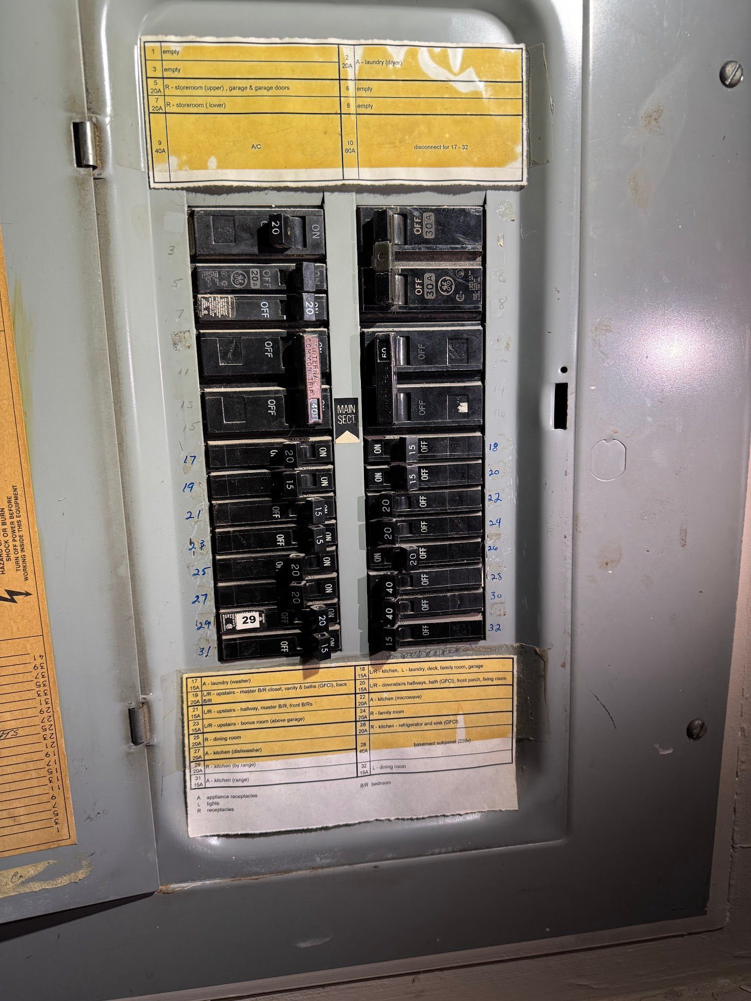 Electrical breaker panel with rows of black switches and yellow labels inside a gray metal cabinet