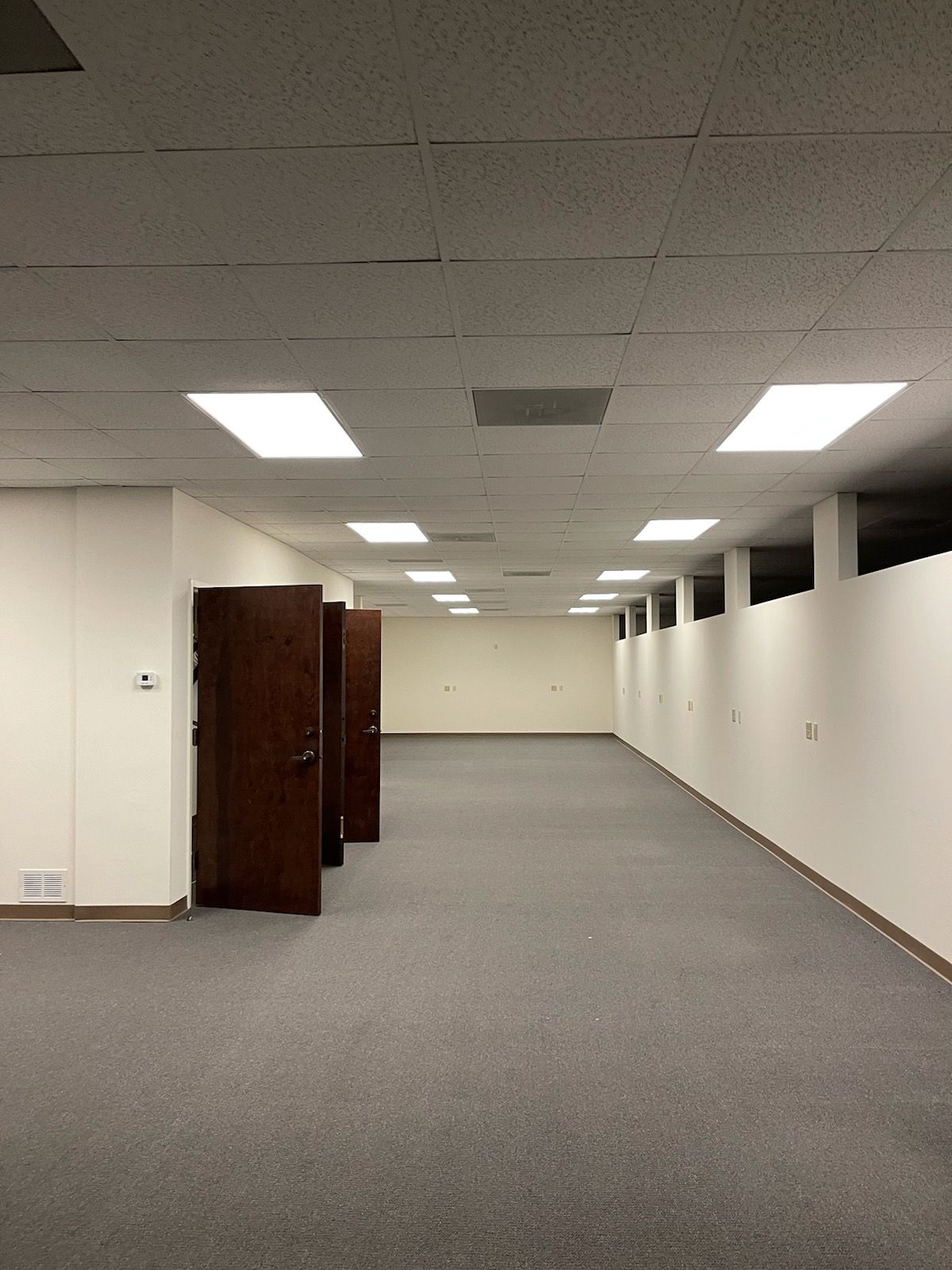 Empty office space with gray carpet, white walls, and fluorescent ceiling lights
