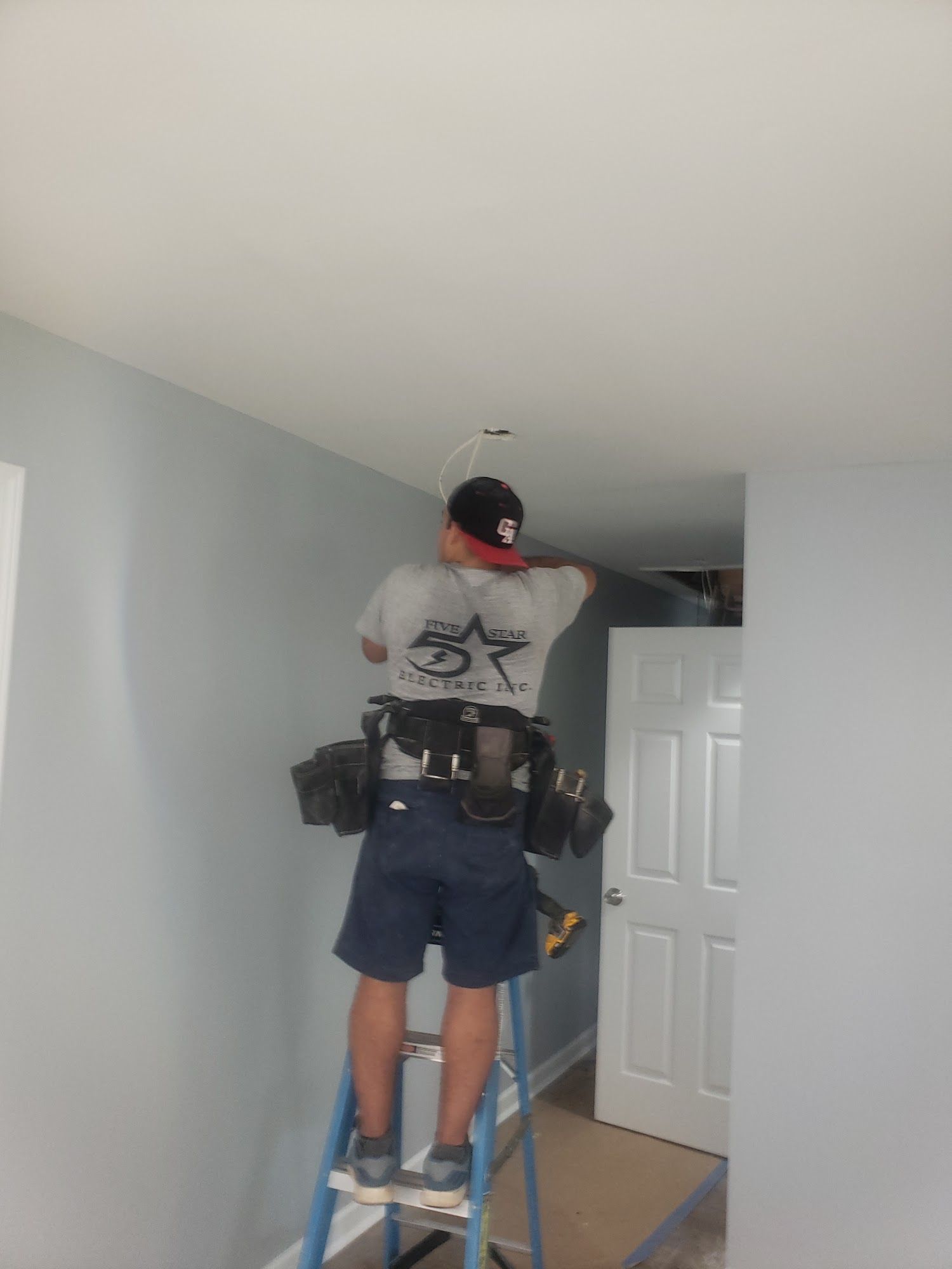 Person standing on a ladder repairing a ceiling light in a hallway.