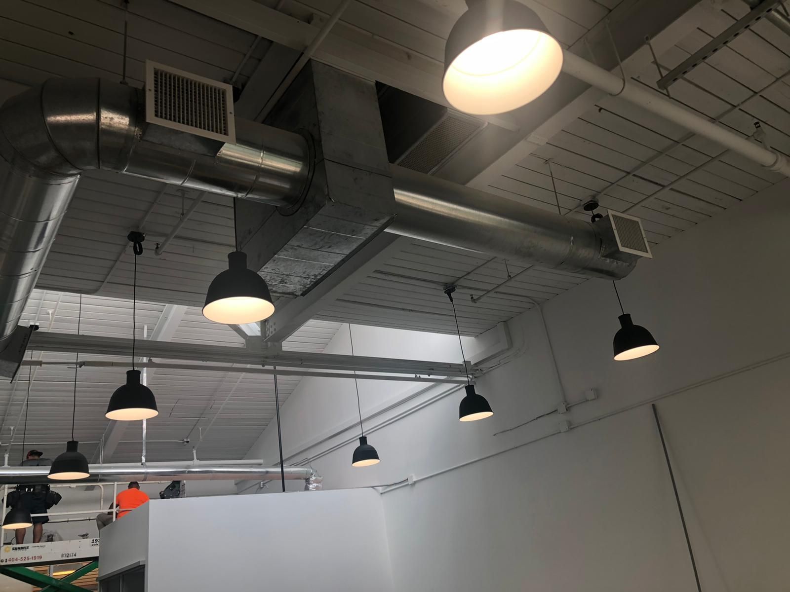 Industrial ceiling with hanging lights, exposed ductwork, and white walls in a warehouse-like room