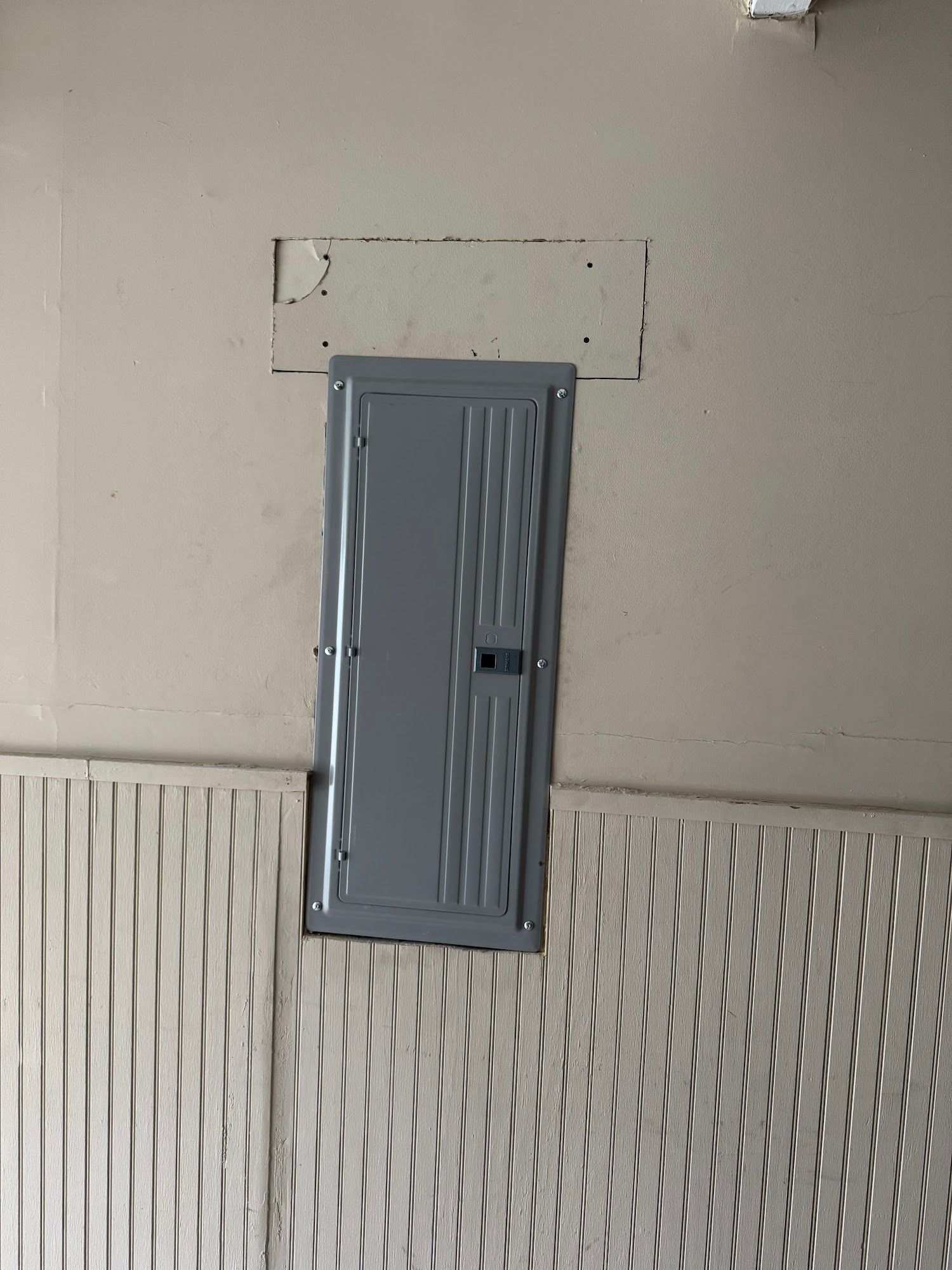 Gray electrical panel on a beige wall above white wainscoting