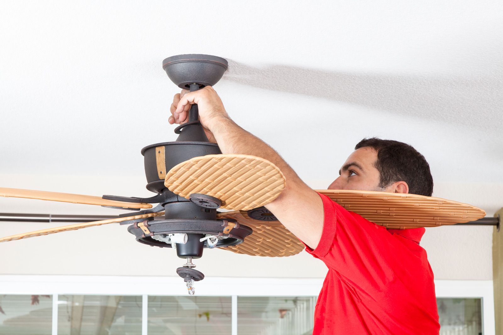 Man tightening a ceiling fan with a tool in a bright room