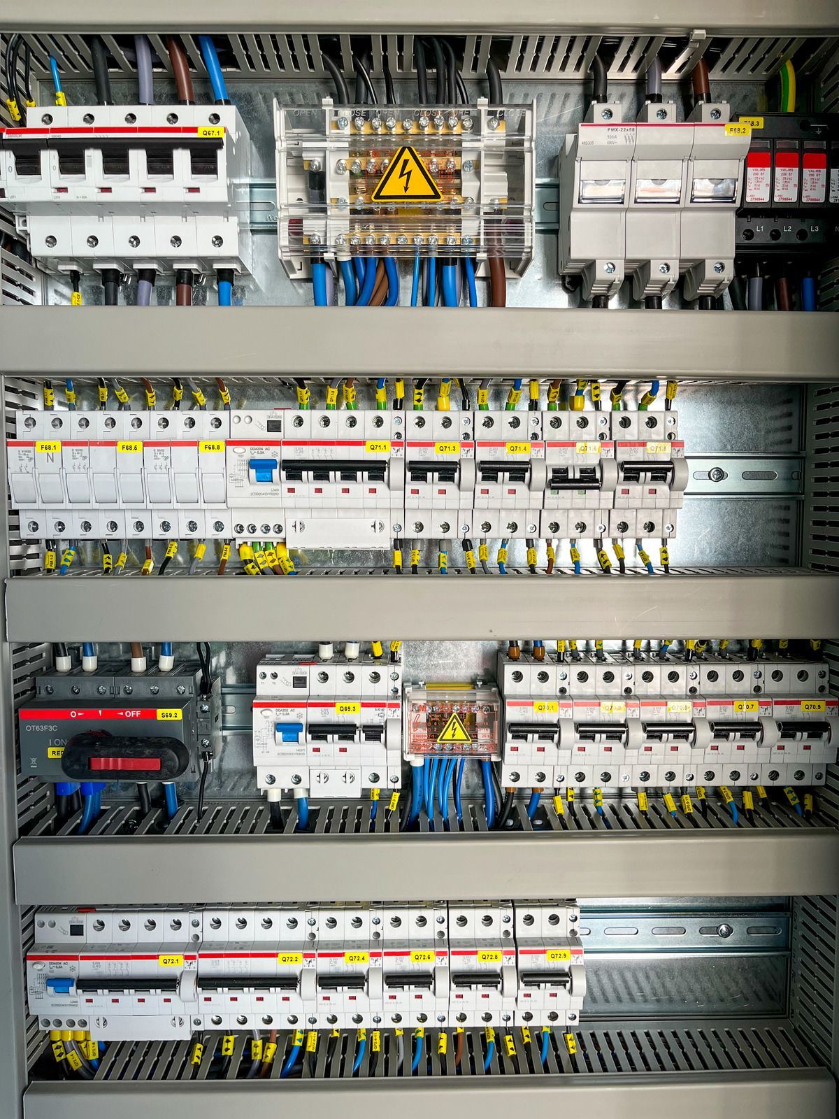 Electrical control panel with rows of circuit breakers, wiring, and warning labels.