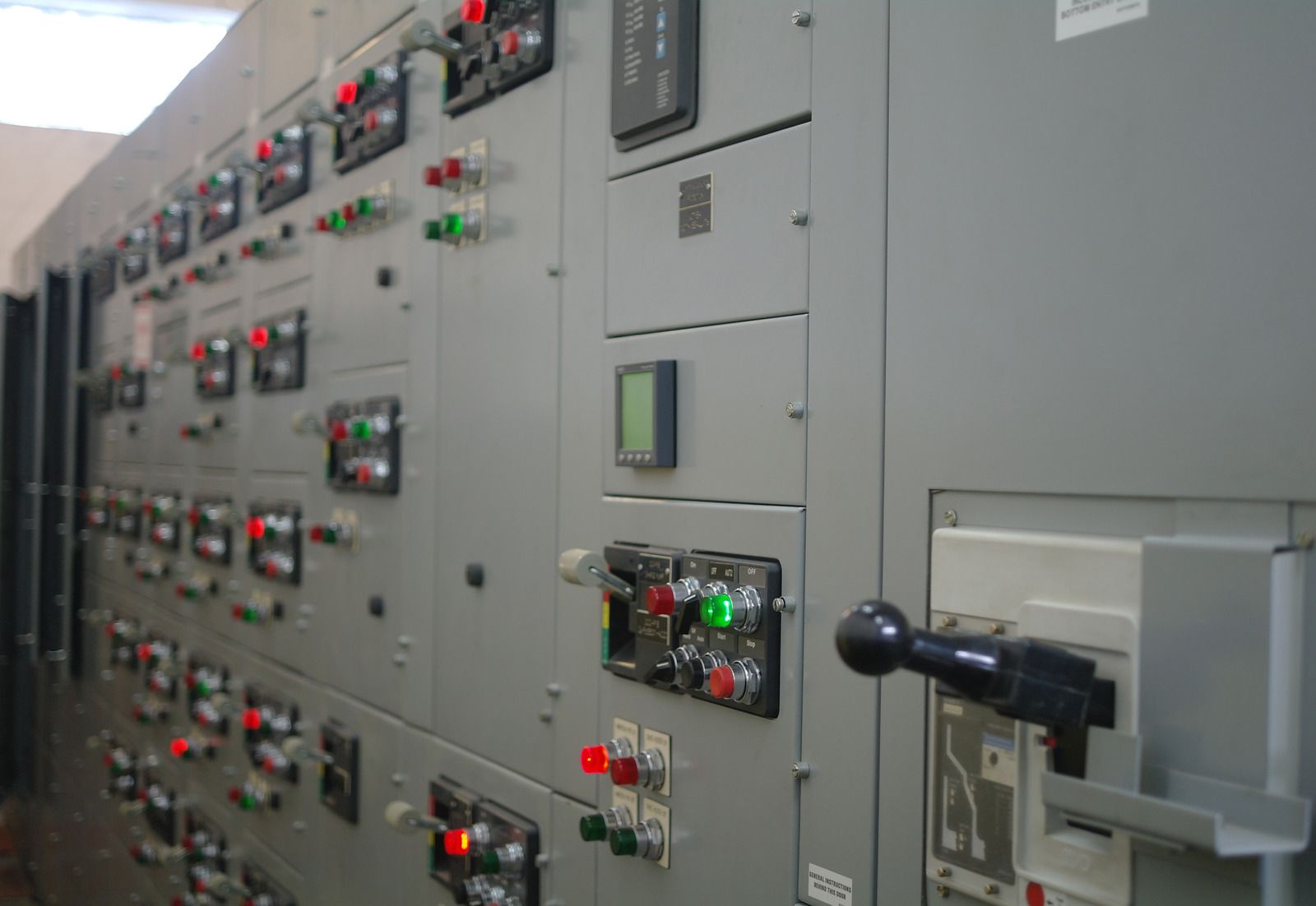 Industrial control panel with rows of switches, lights, and gauges on a gray wall