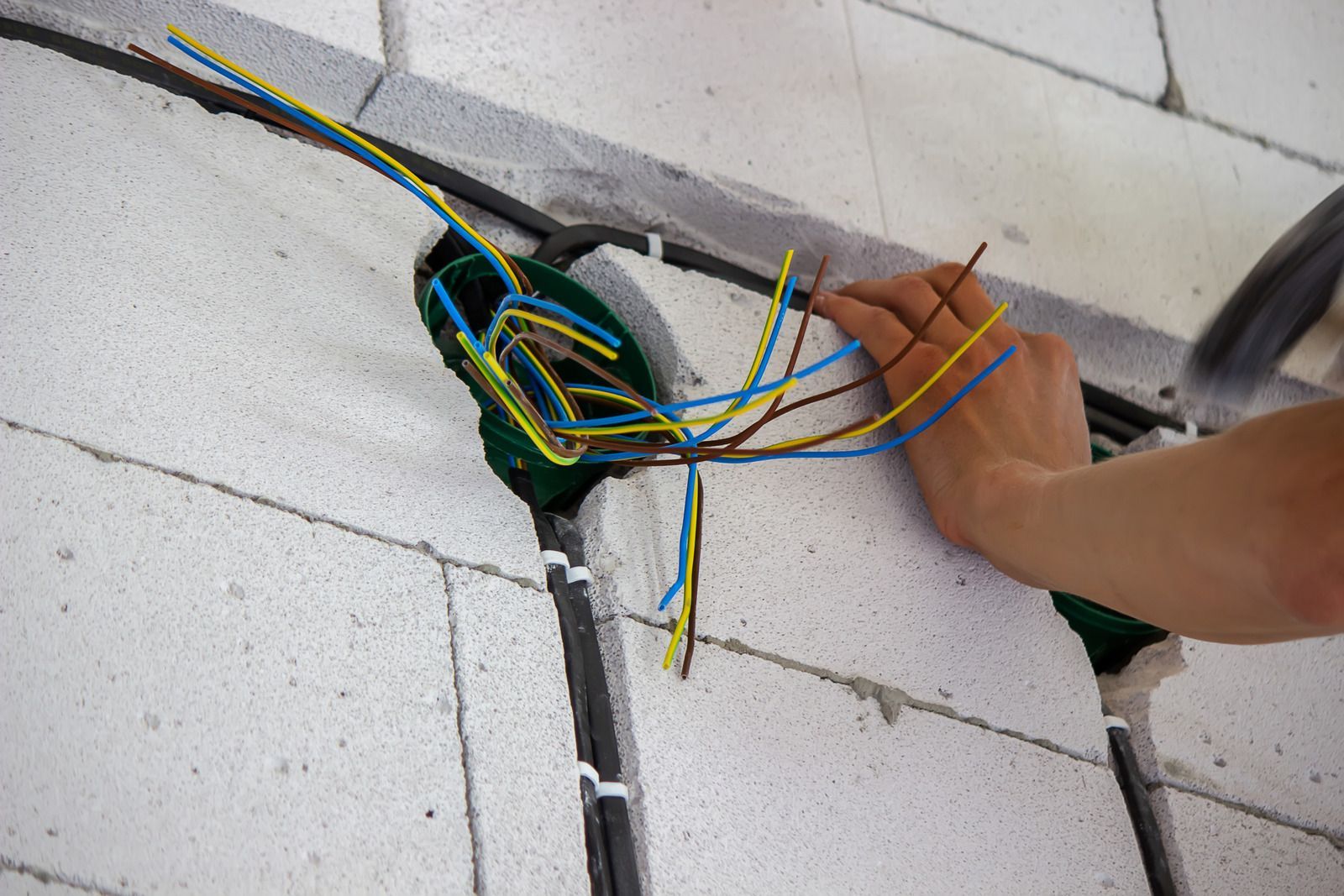 Electrical wires bundled in a wall cavity while a hand adjusts them during installation
