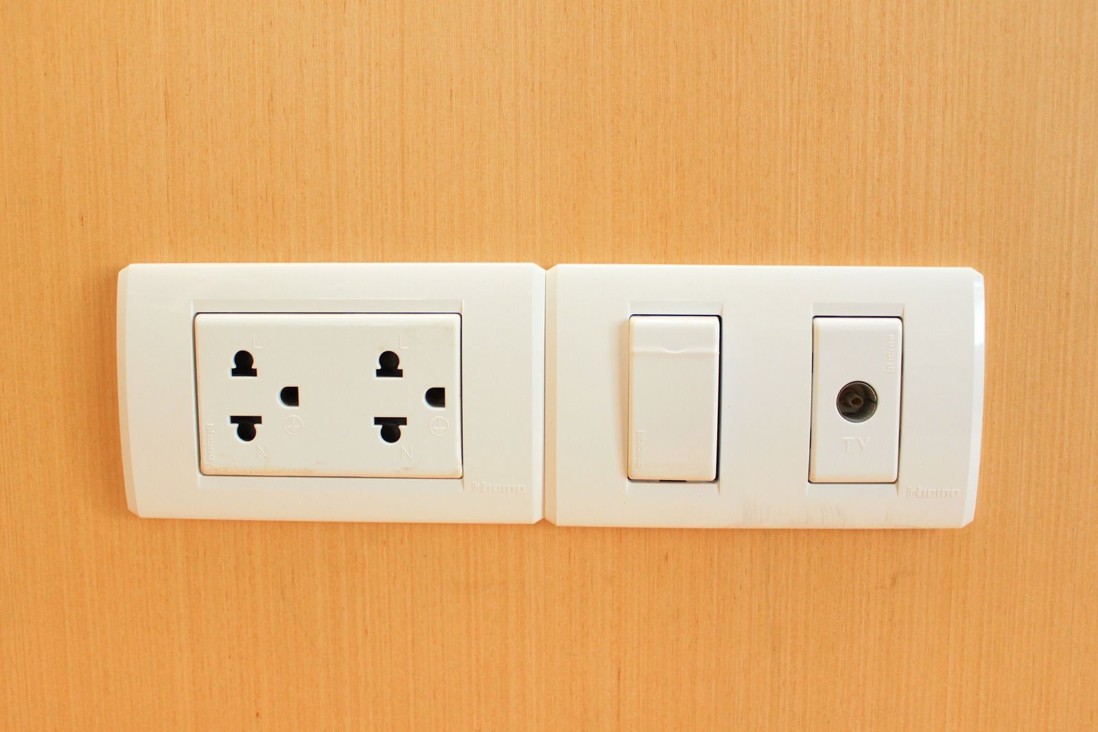 White electrical outlet and switches on an orange wall.