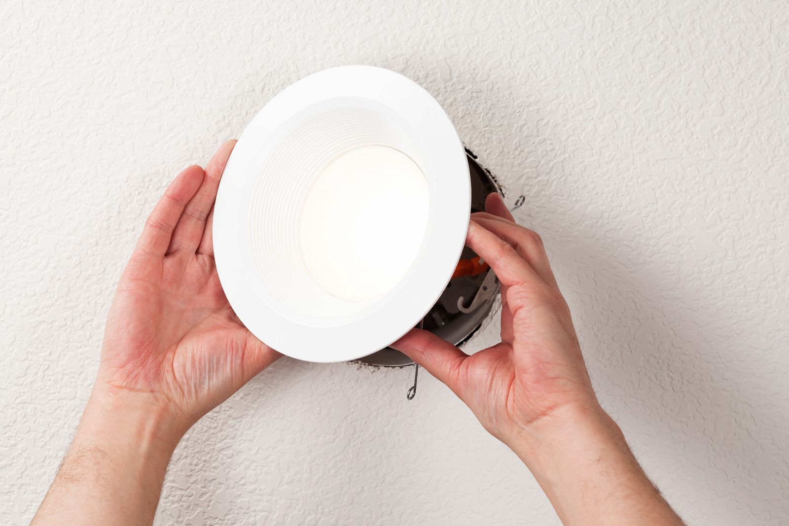 Hands holding a white plate over a wall opening with exposed wiring