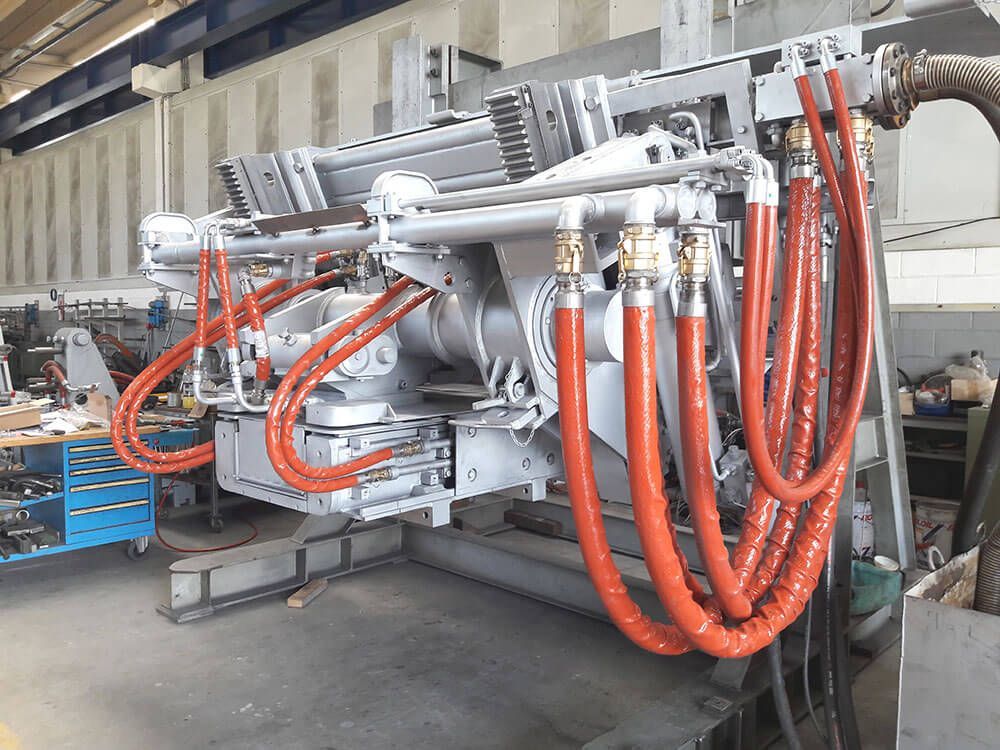 Grande macchina industriale con tubi rossi e carrozzeria argentata in un ambiente da officina.