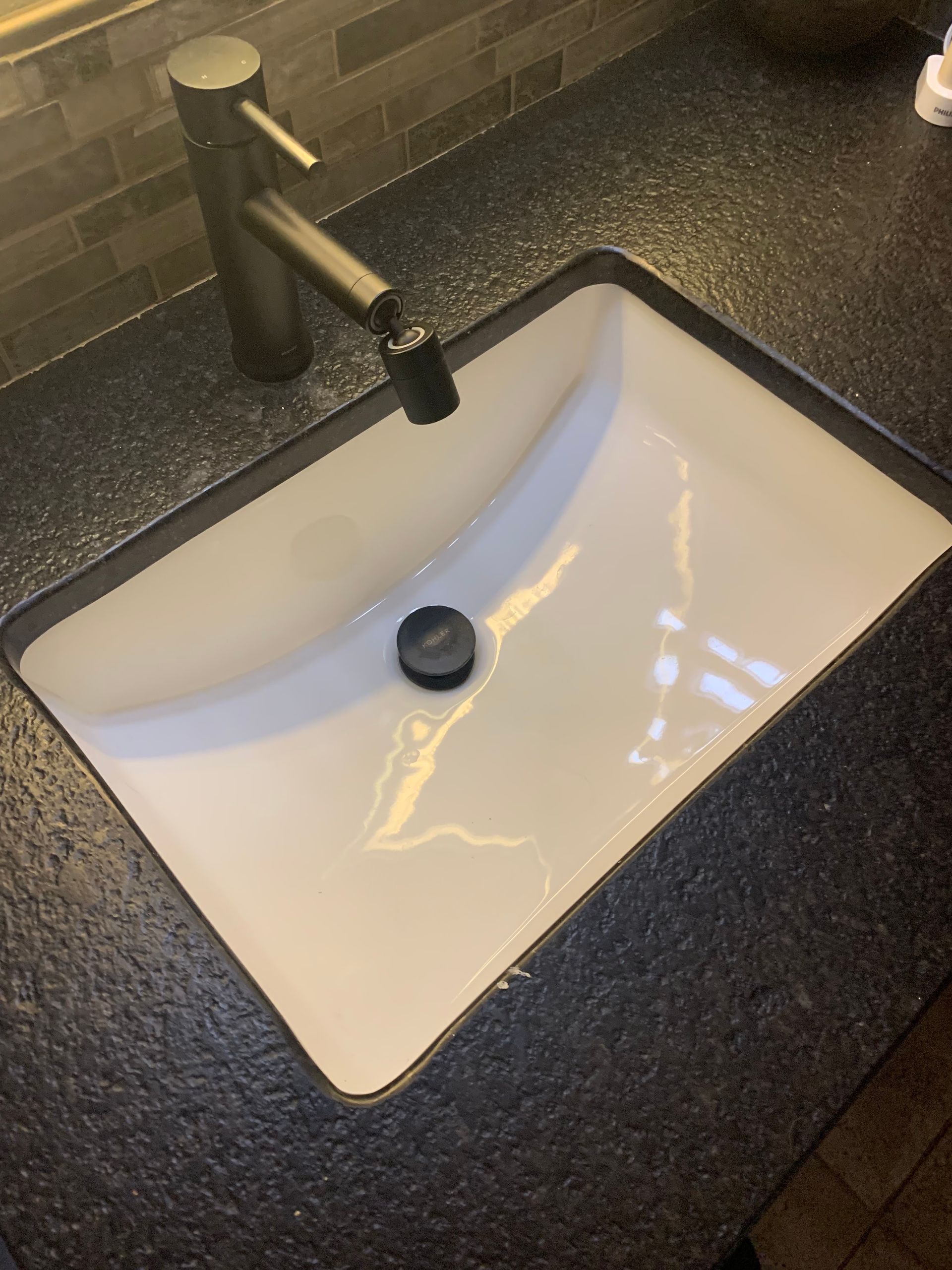 White rectangular sink in black countertop with black faucet.