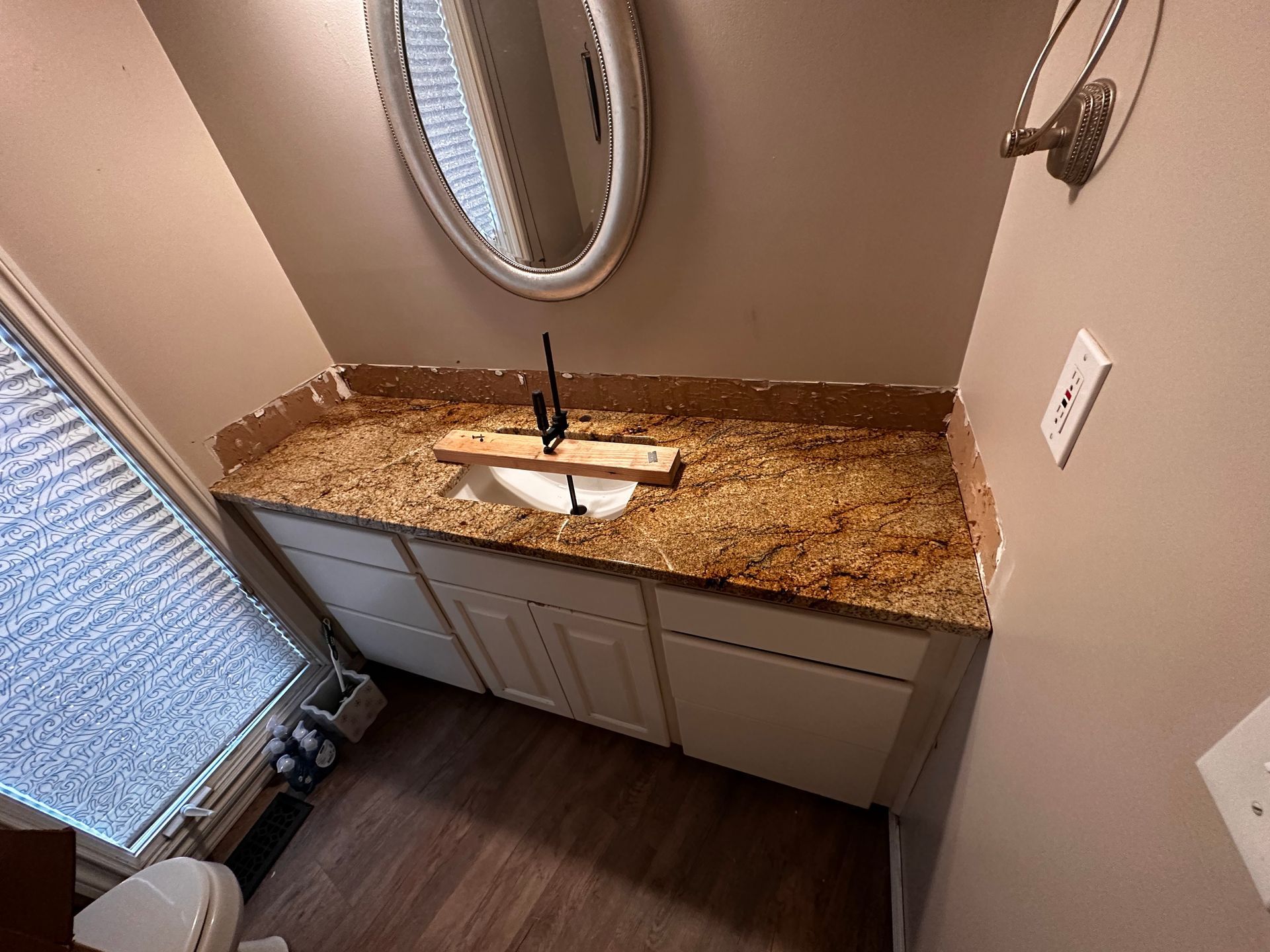 Bathroom with white cabinets, granite countertop, oval mirror, and black faucet.