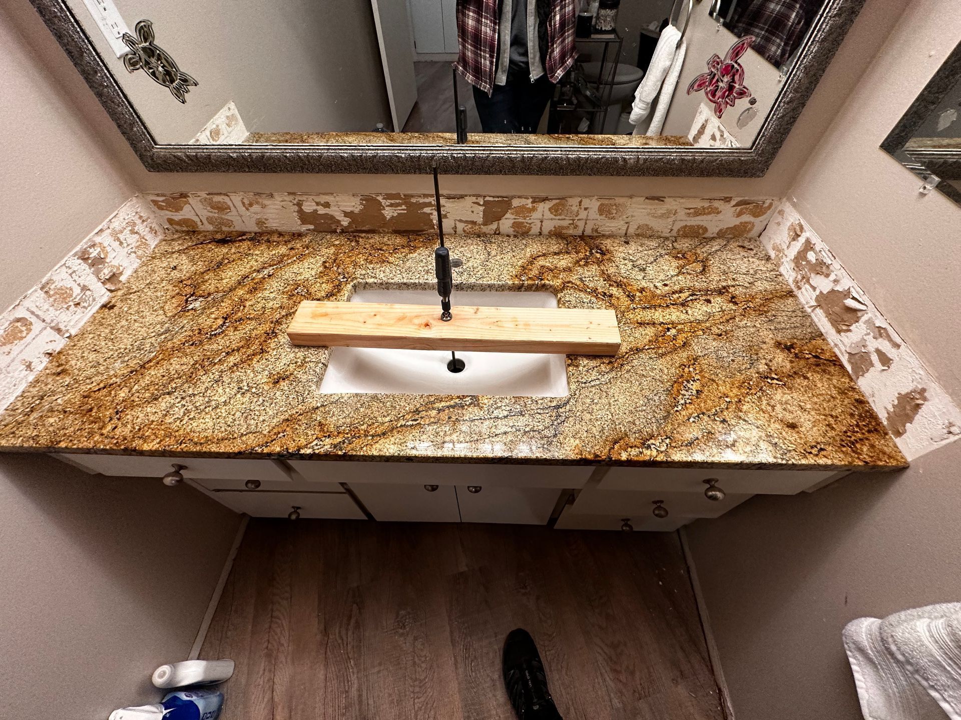 Bathroom with gold granite countertop, white sink, and framed mirror. Wall damage visible.